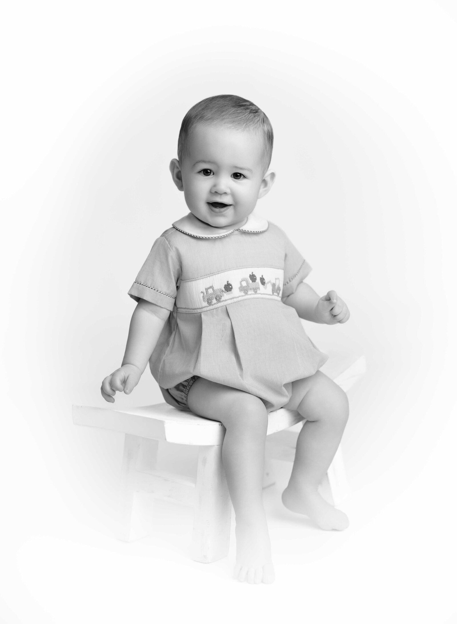 Baby on white stool smiling at camera for a B&W heirloom baby portrait. Heirloom photo taken by Jenni Nikki Photography in Atlanta, GA.