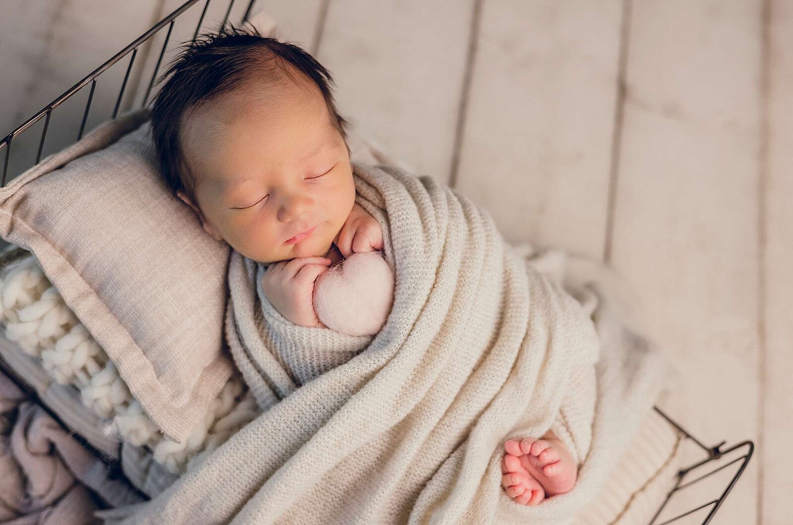 A peaceful newborn boy sleeping in a woven basket, holding a felt heart, captured by Bia Schaefer, Orlando's top in in-home newborn photographer.