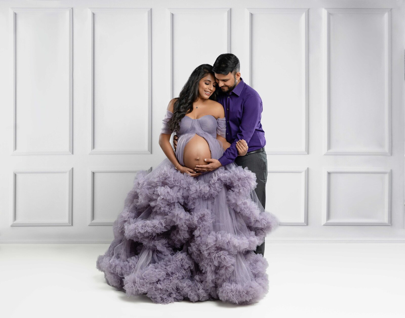Mom and Dad wearing purple and cuddling as they look at baby bump. 