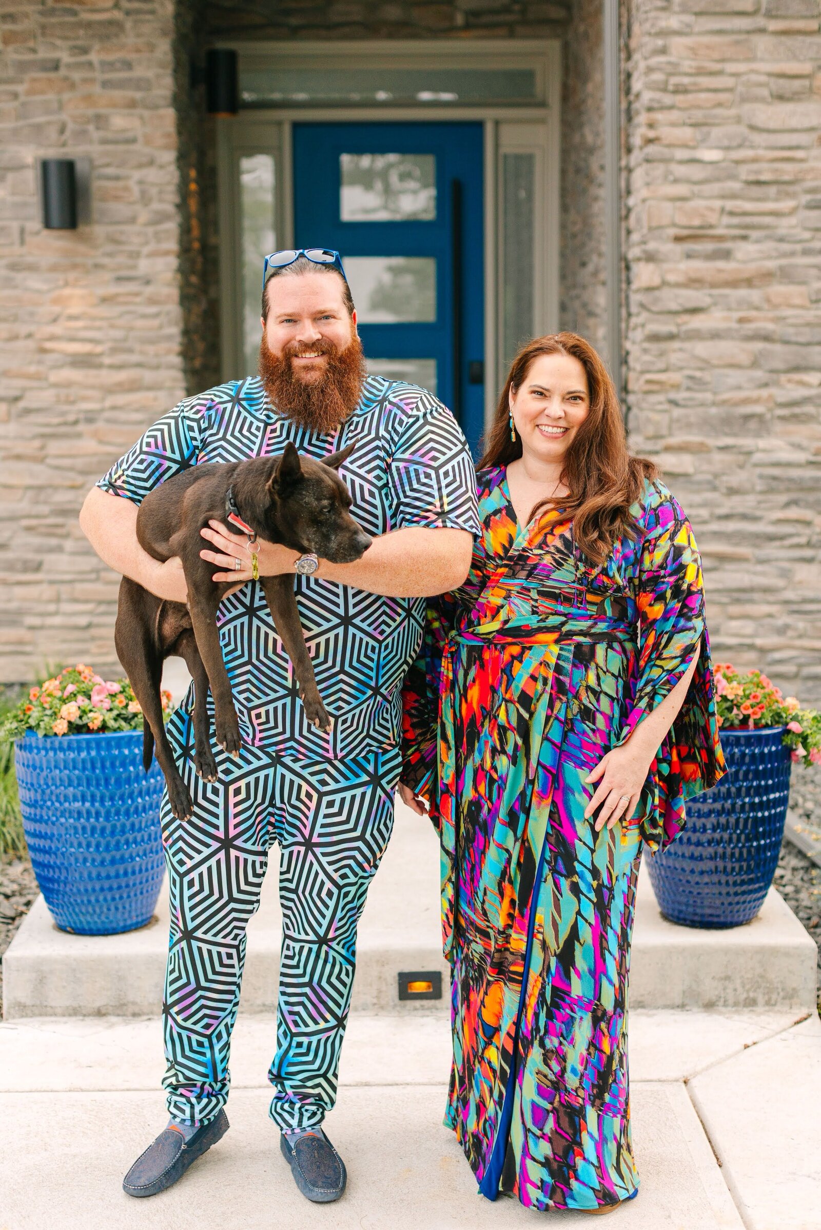 Two people standing in front of a house while one holds a dog.