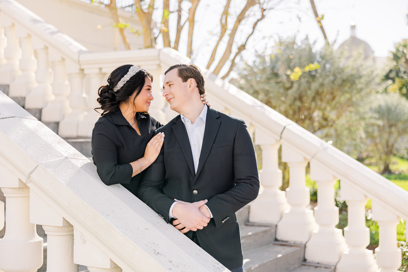 An interracial couple look into eachother's eyes while standing on a white staircase