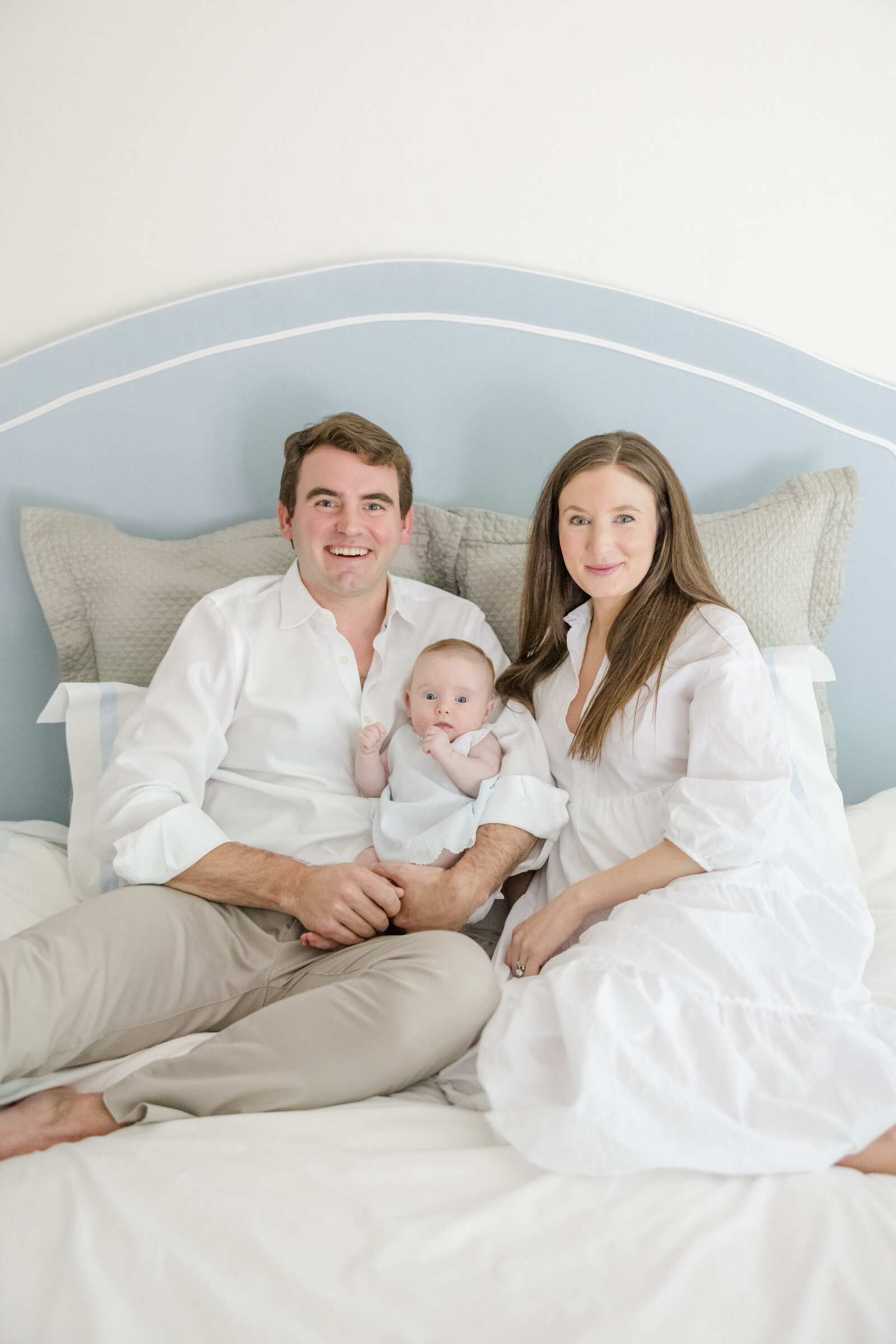 Parents seated in front of a blue headboard holding their baby.
