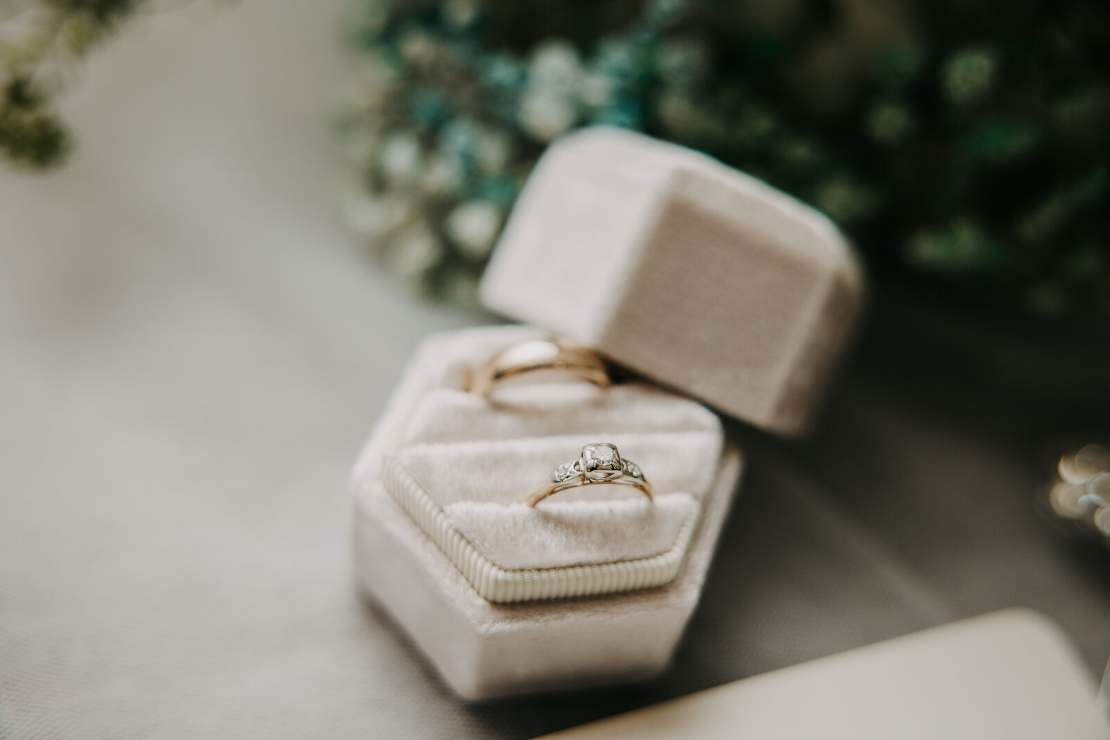 Wedding rings in a white velvet ring box, set in front of a bridal bouquet for an elegant and romantic detail shot.