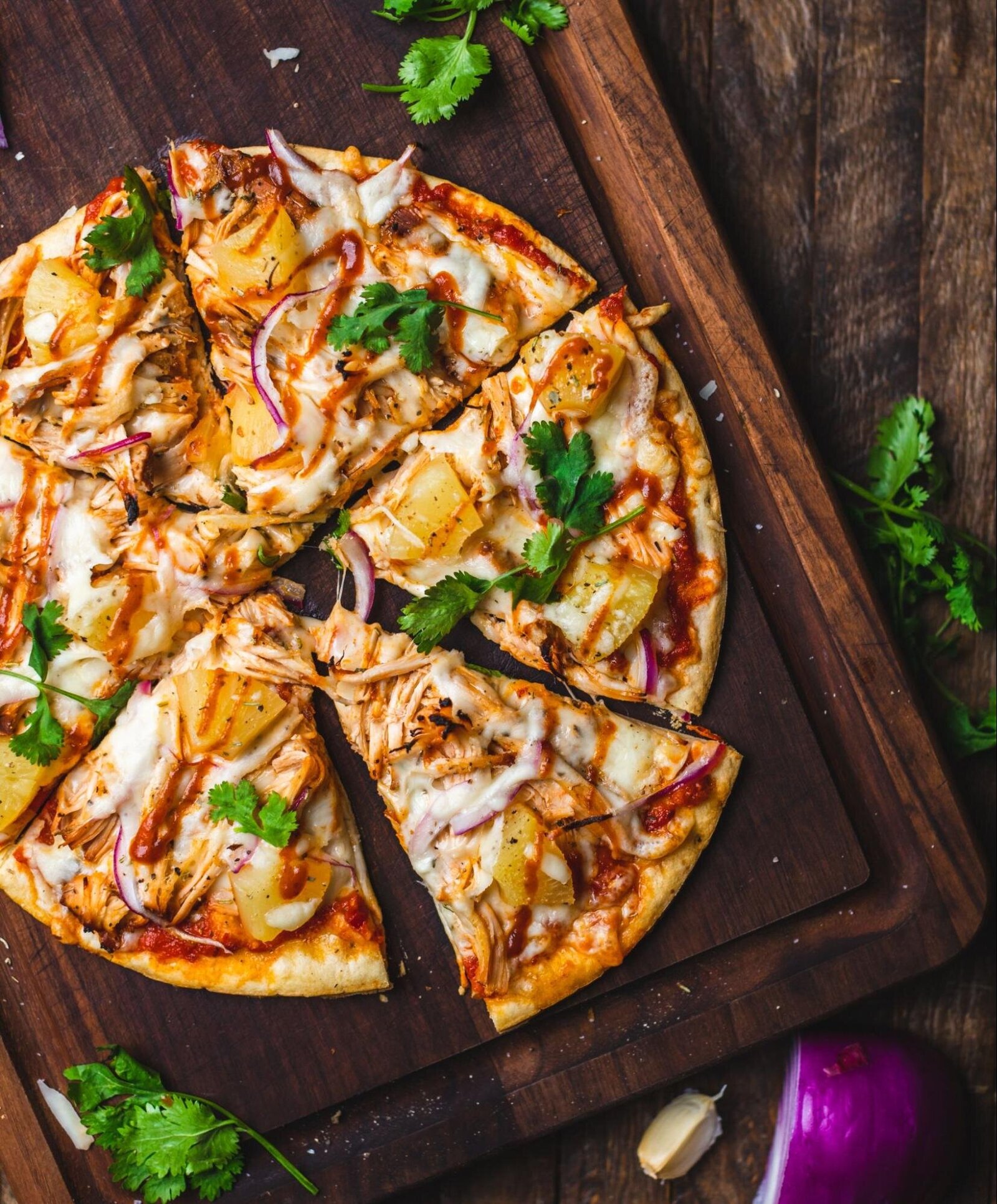 Image: cheese pizza with grilled pineapple and onion on a brown cutting board