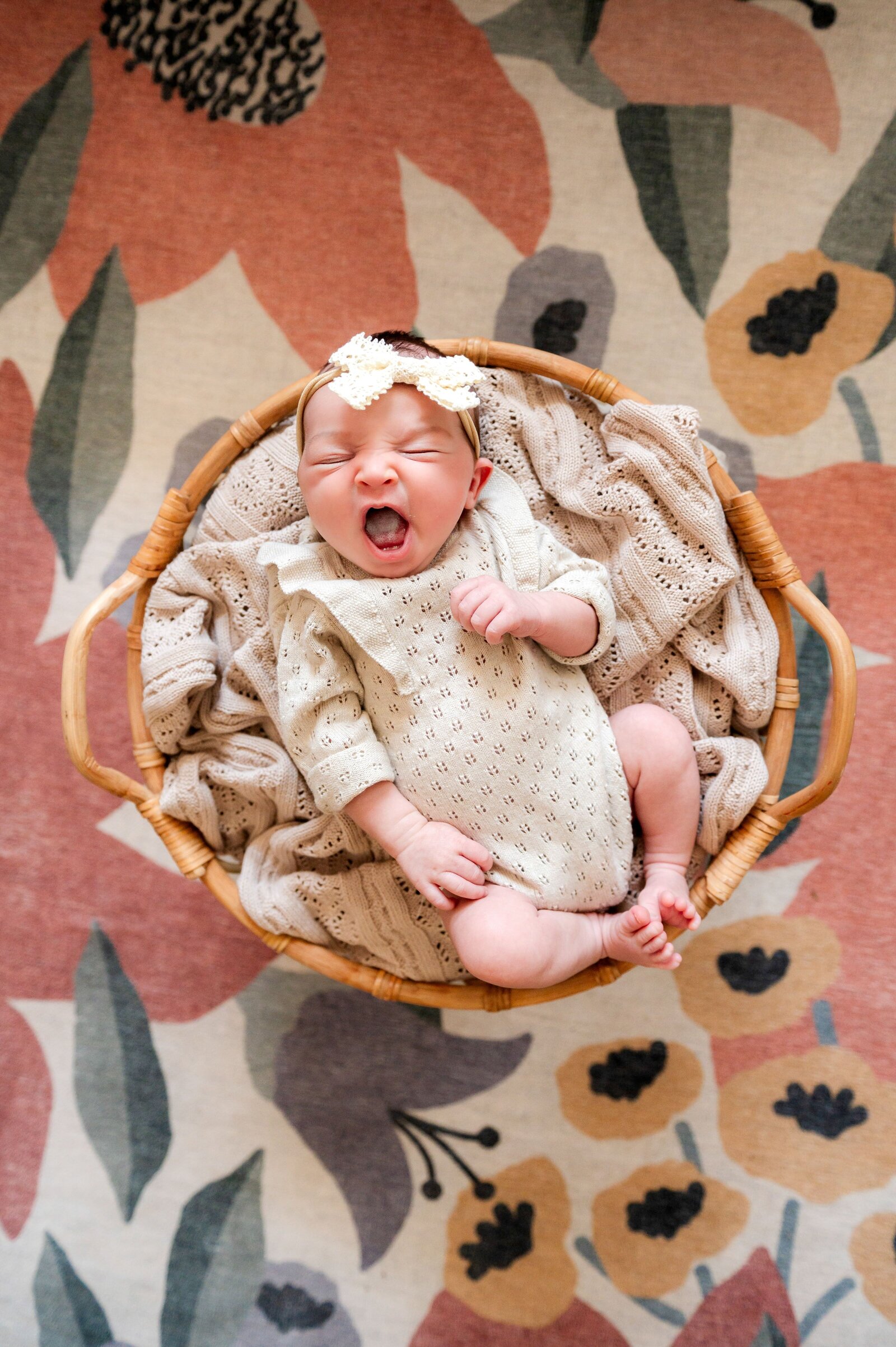 newborn yawning in a basket with a cream blanket