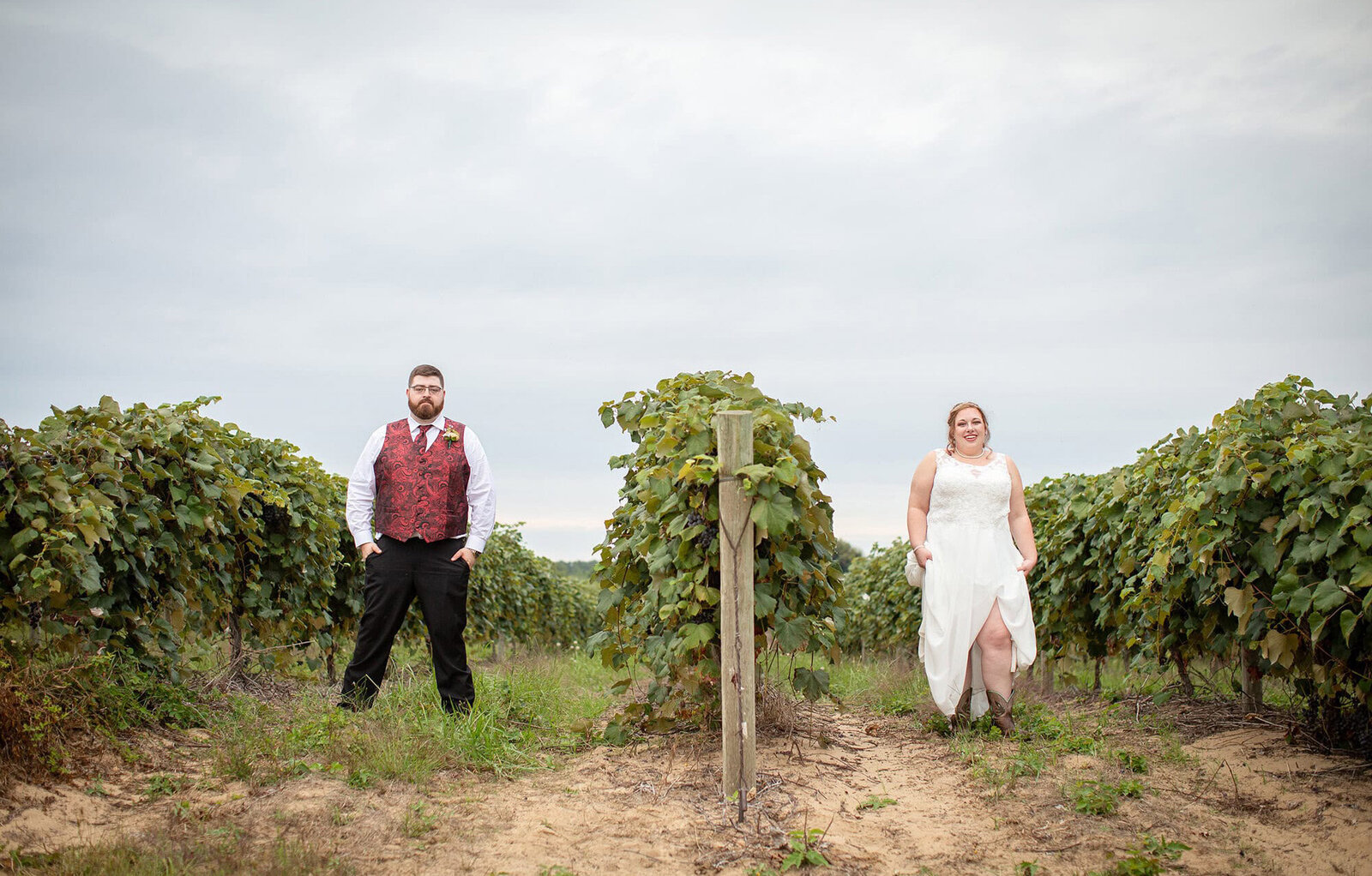 wedding couple pose in two rows of grapevines