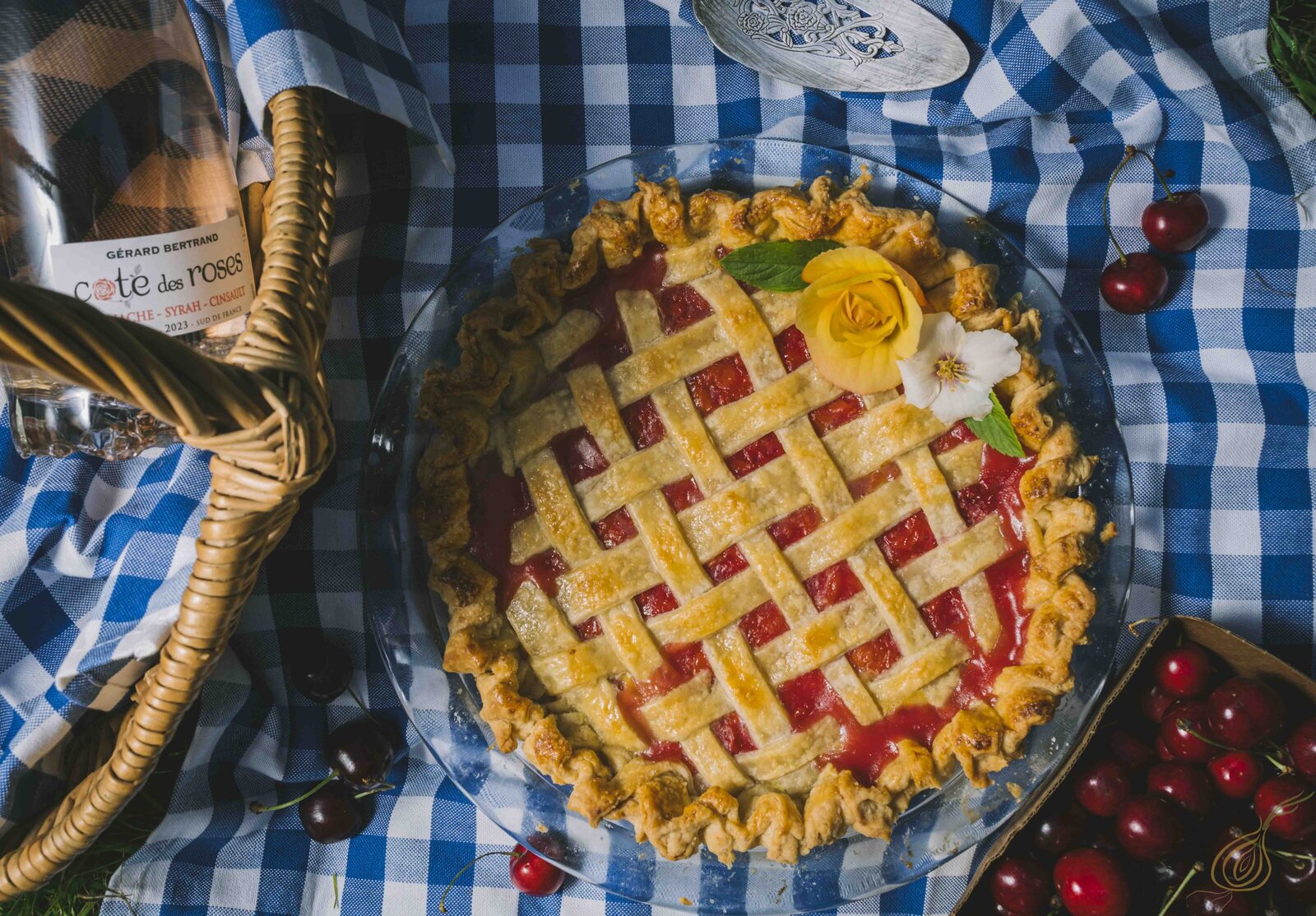 A delicious cherry pie sits beside a basket filled with fresh, ripe cherries, showcasing a vibrant red color.