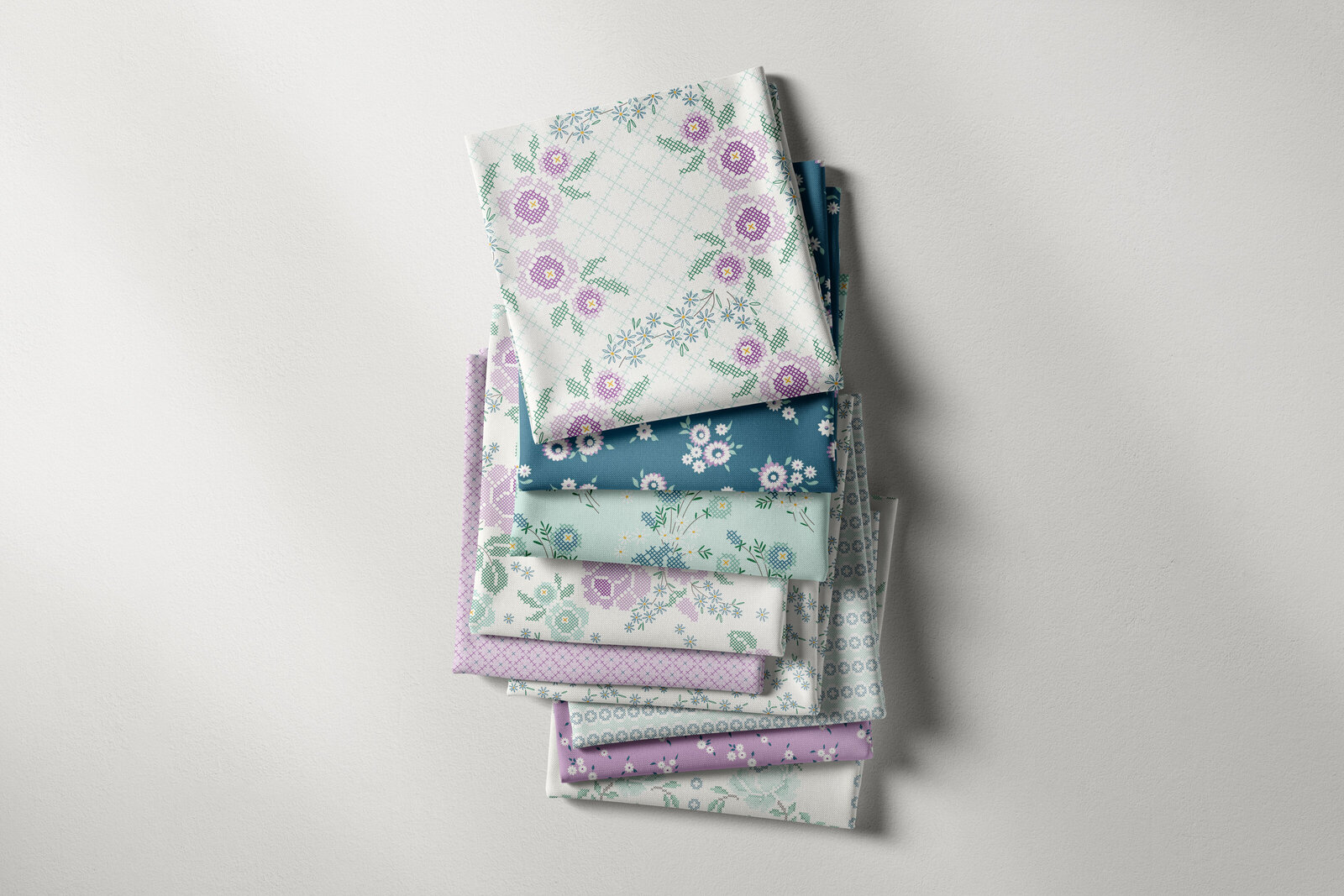 Stack of folded fabrics with floral cross stitch designs printed on them.
