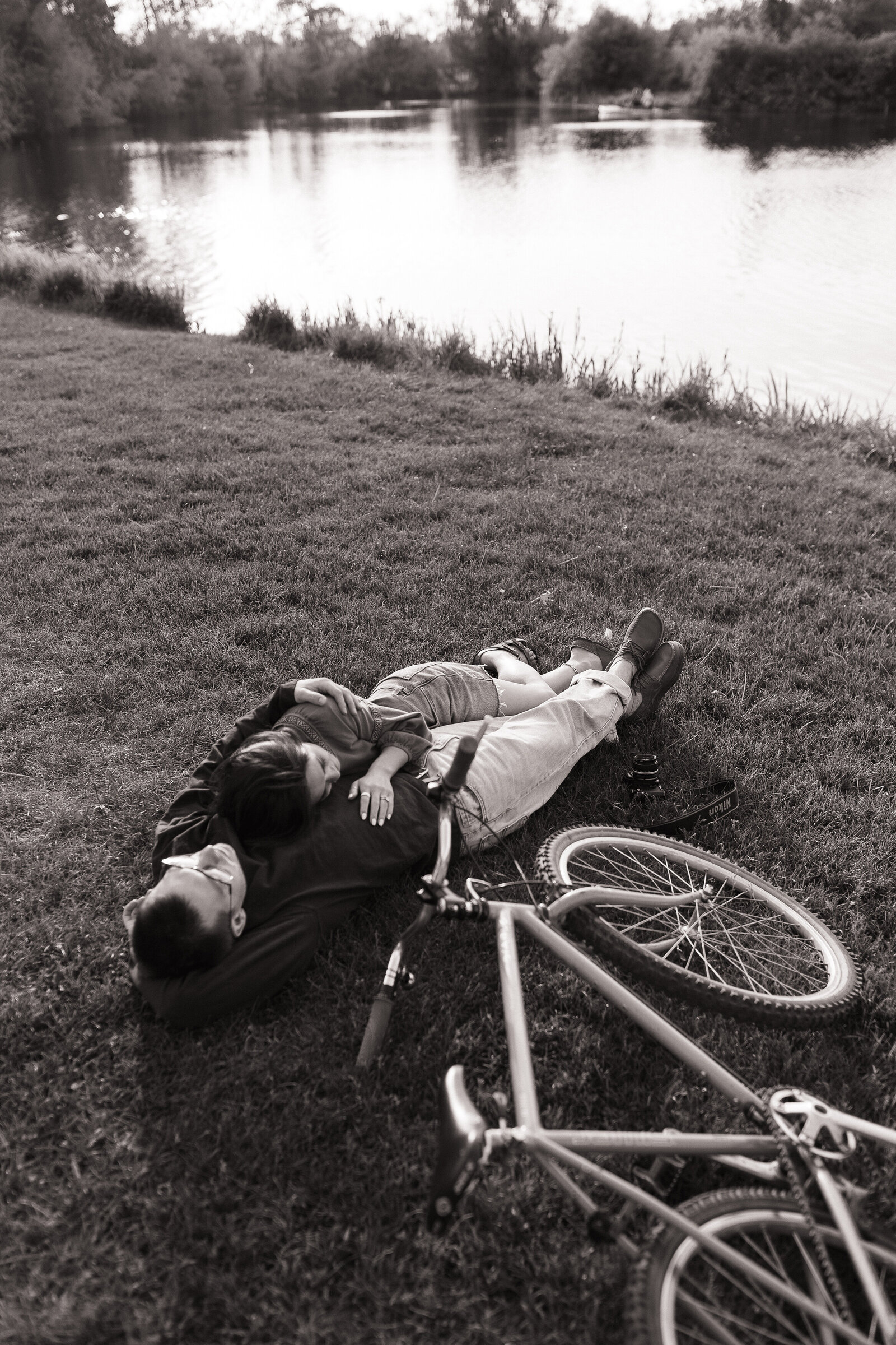 Cozy photo of couple laying in grass beside bicycle in nature