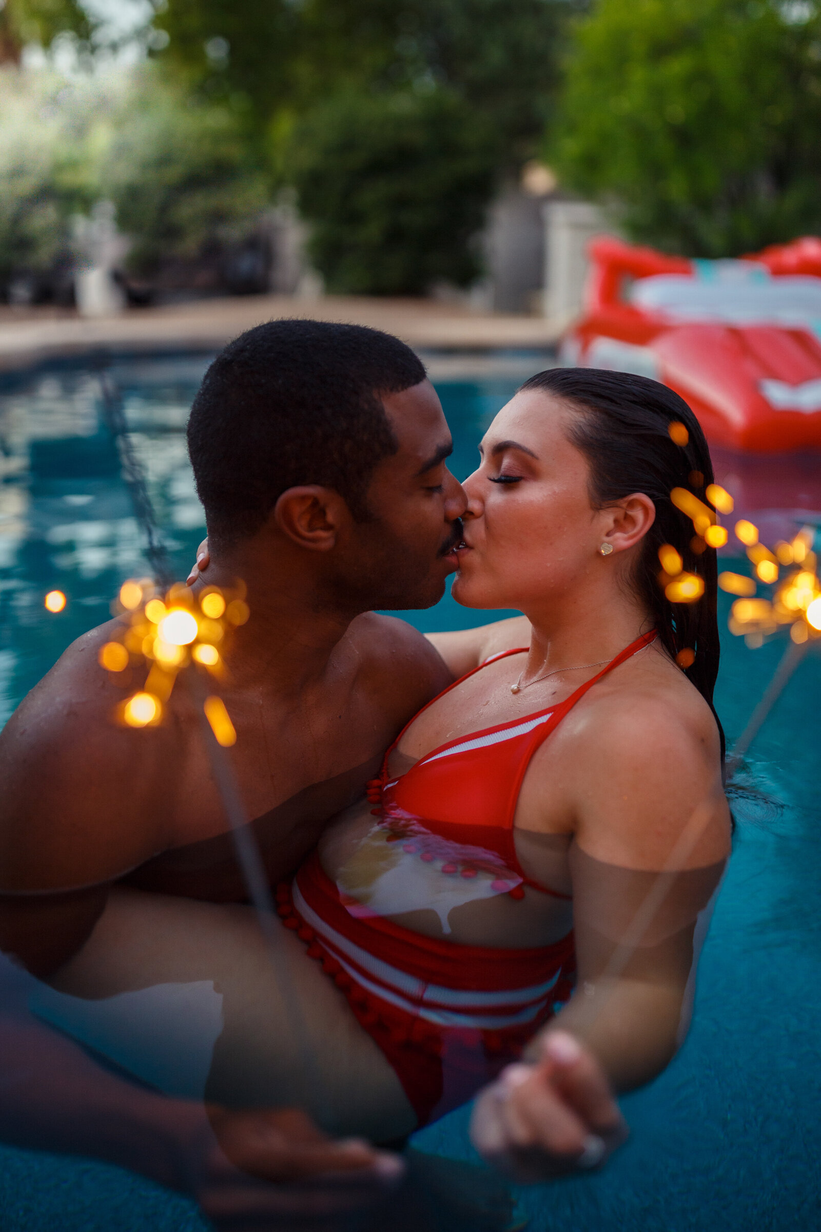 couple kissing in pool holding sparklers
