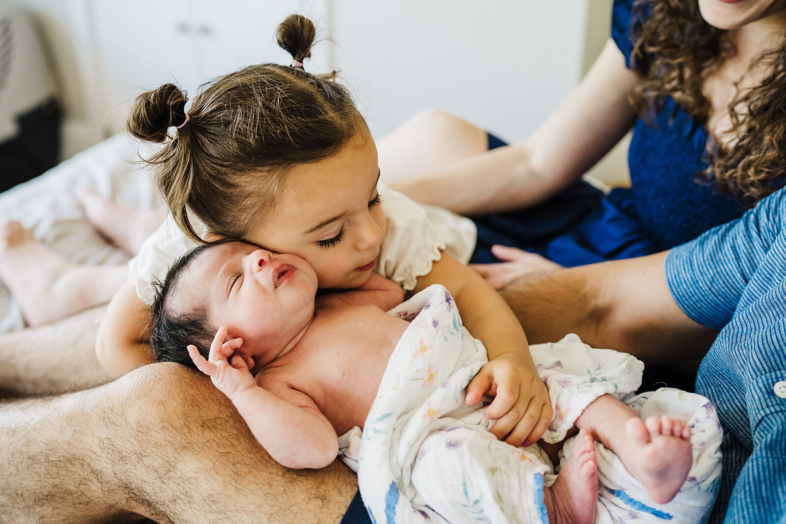 toddler sister with pigtails hugs newborn baby sister during boston family photos