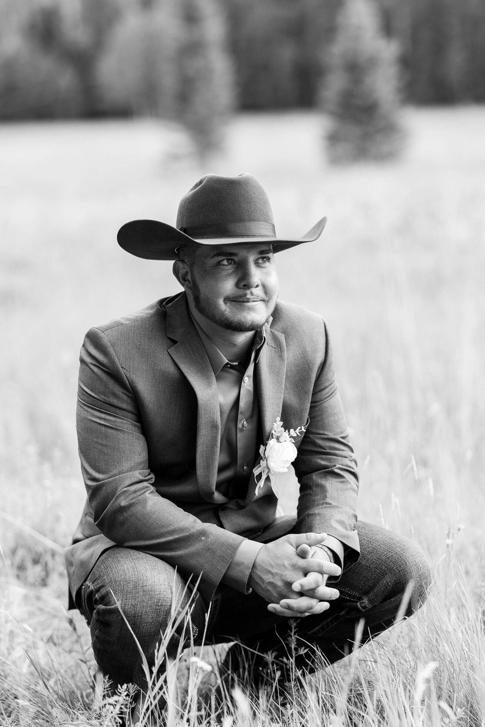 Black and white photo of groom squatting down for portrait in the grass field