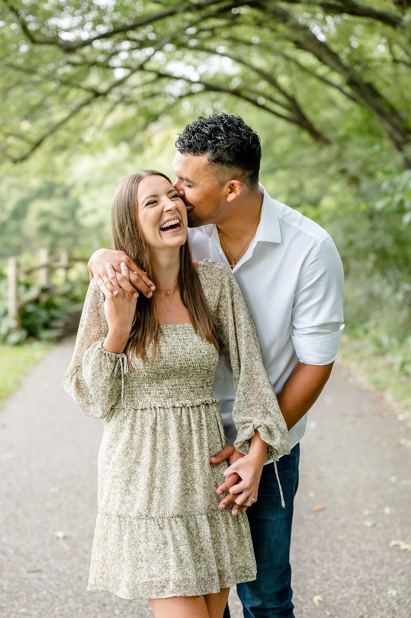 Engaged-couple-laughing-as-the-guy-whispers-in-his-fiances-ear-and-kisses-her-on-the-cheek