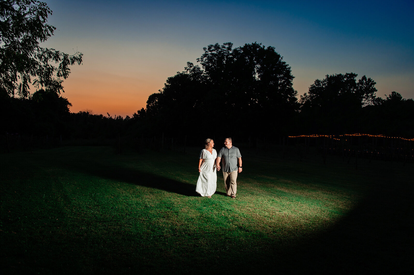 Couple walking through an open field at sunset, dramatic lighting in field