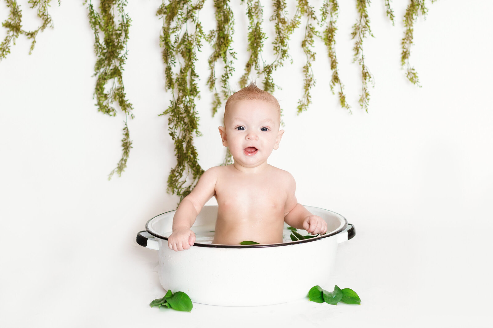 Milestone Photographer, a baby sits in a ceramic pot with leaves surrounding it