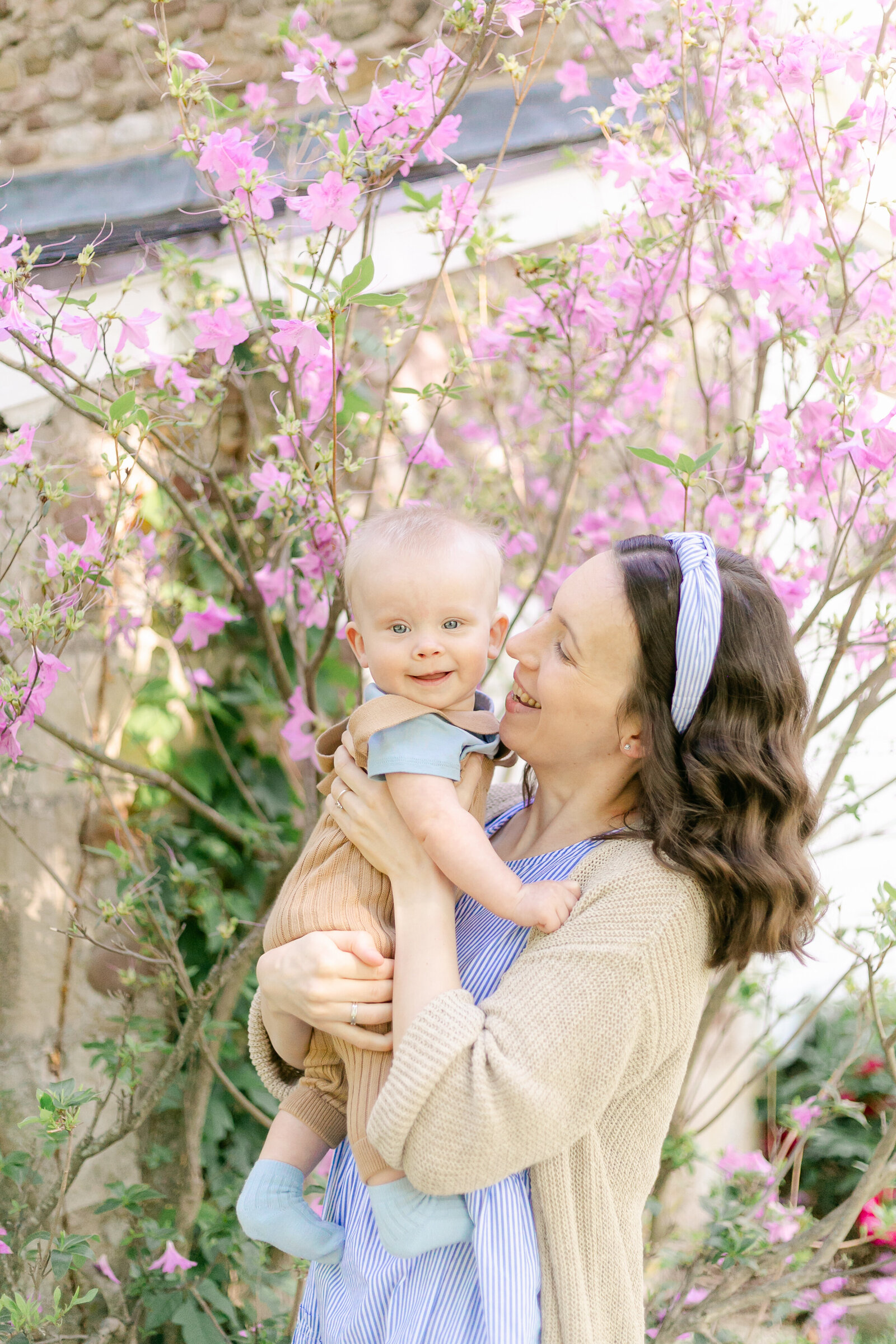 A baby and his mother snuggle in front of a pink flowering tree during Emi Rose's Rochester NY Motherhood Photography sessions.