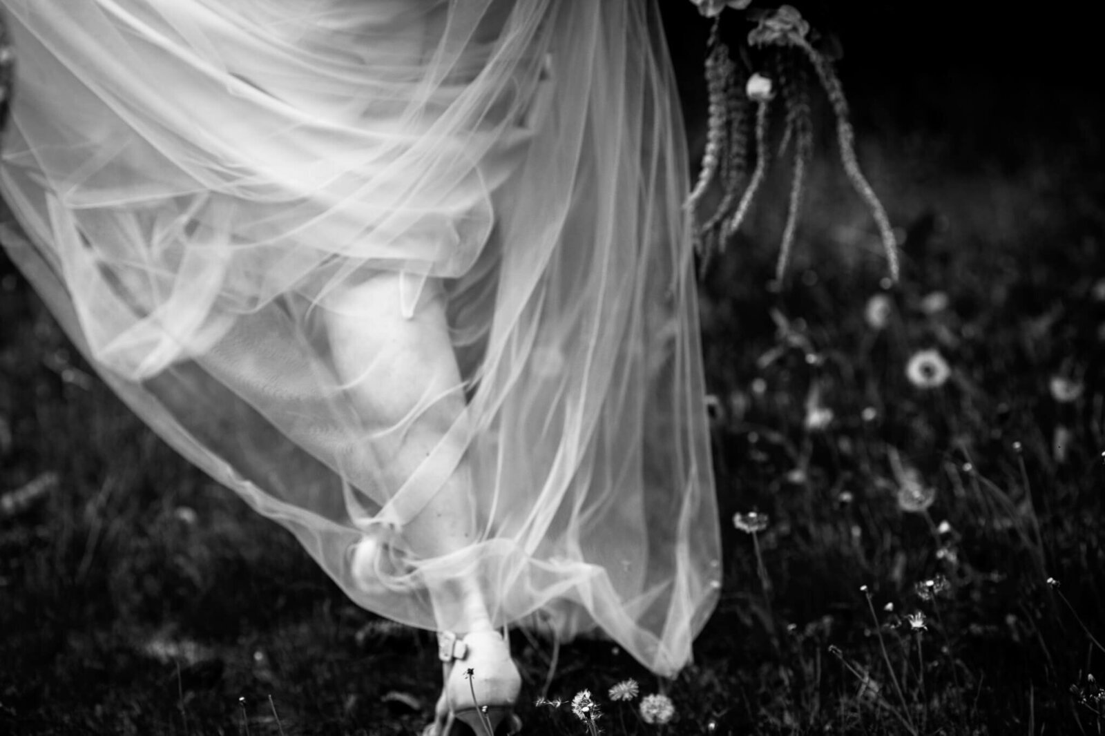 closeup of wedding dress and shoes as bride walks through a field of wildflowers.