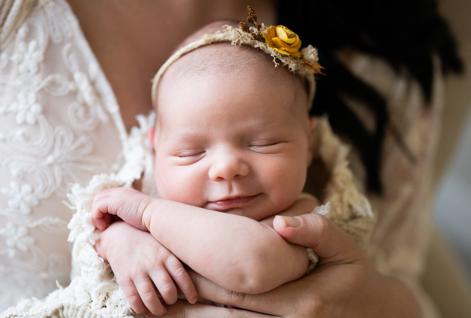 Newborn Baby smiling in her sleep with a yellow floral headband.