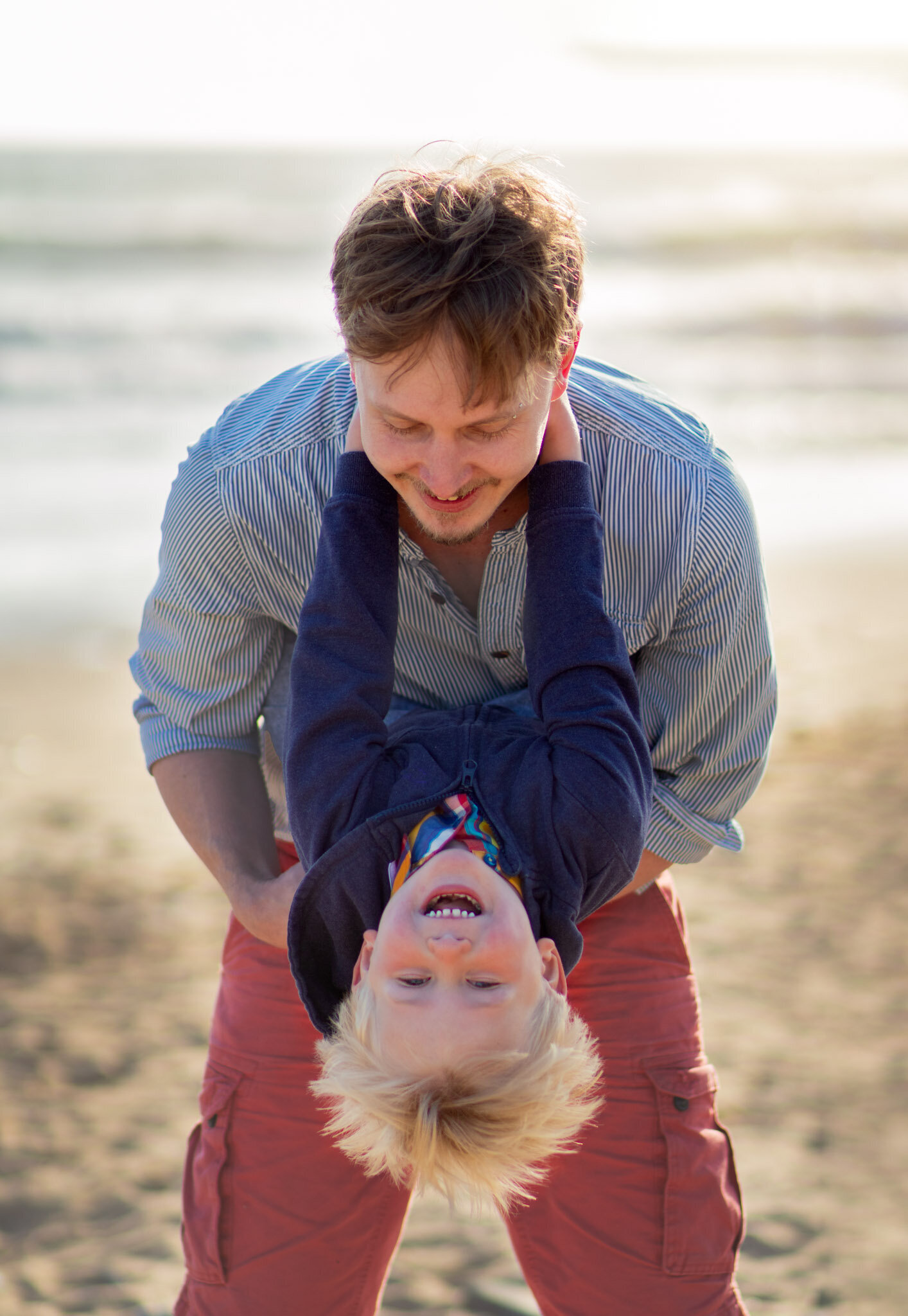 Boy hangs upside down for fun picture in Family photoshoot on the beach in Devon