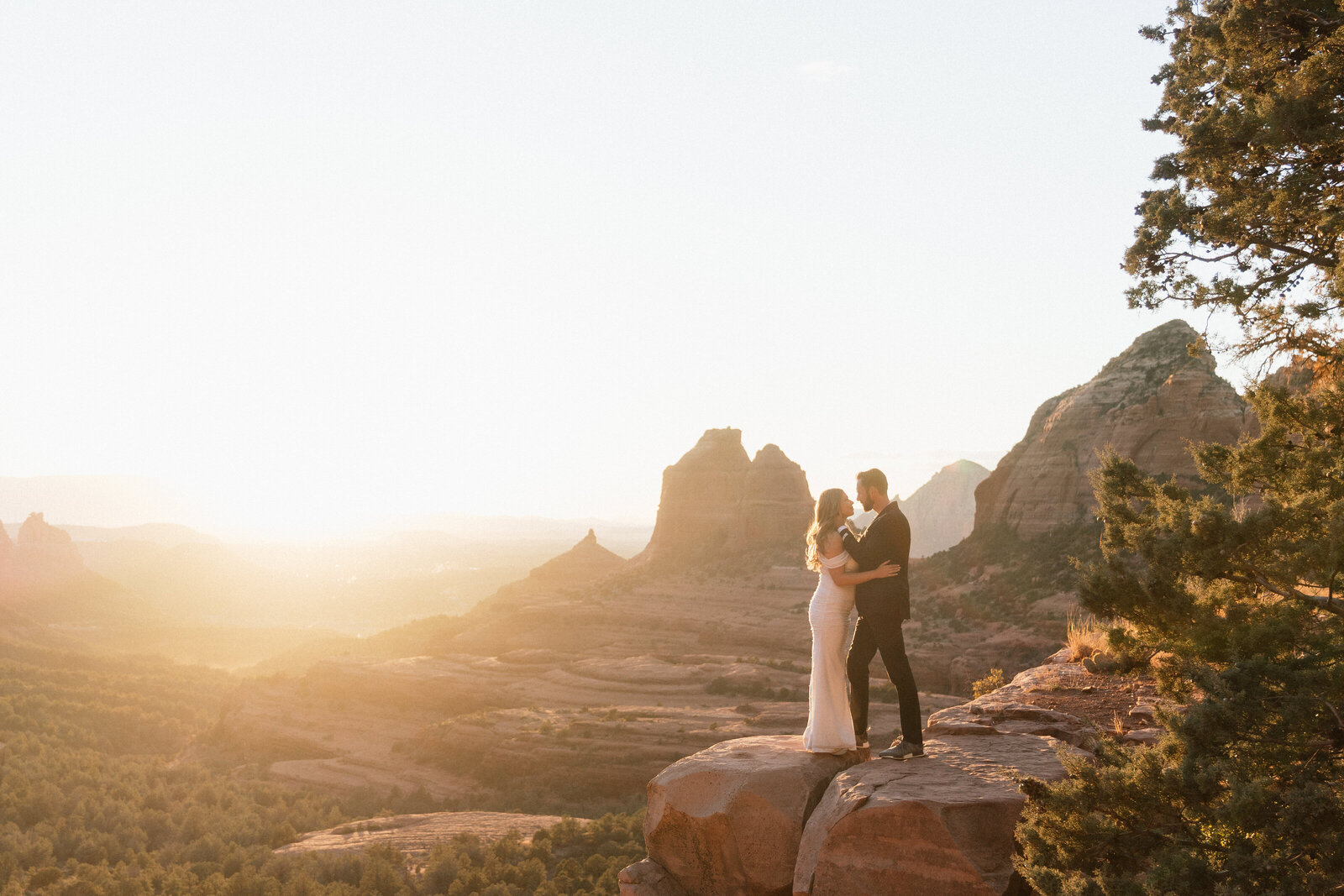 Bride and groom embracing on a red rock cliff at sunset during their Sedona elopement at Merry Go Round Rock.