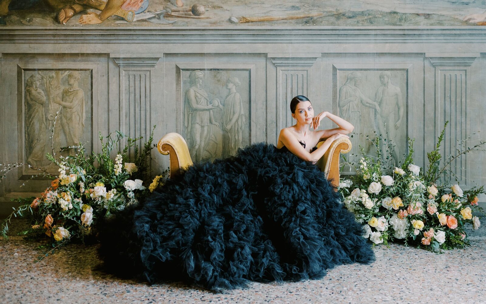 a-woman-in-a-blackgown-sits-on-a-chair-in-front-of-flowers-2