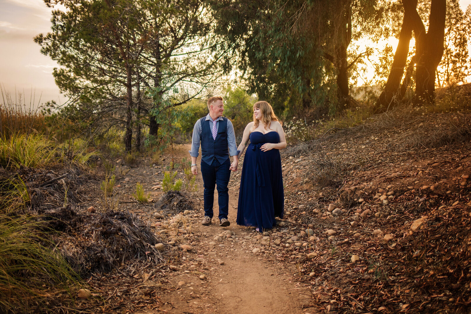 Maternity Photographer, a couple walks together on a trail ion nice attire, she is expecting
