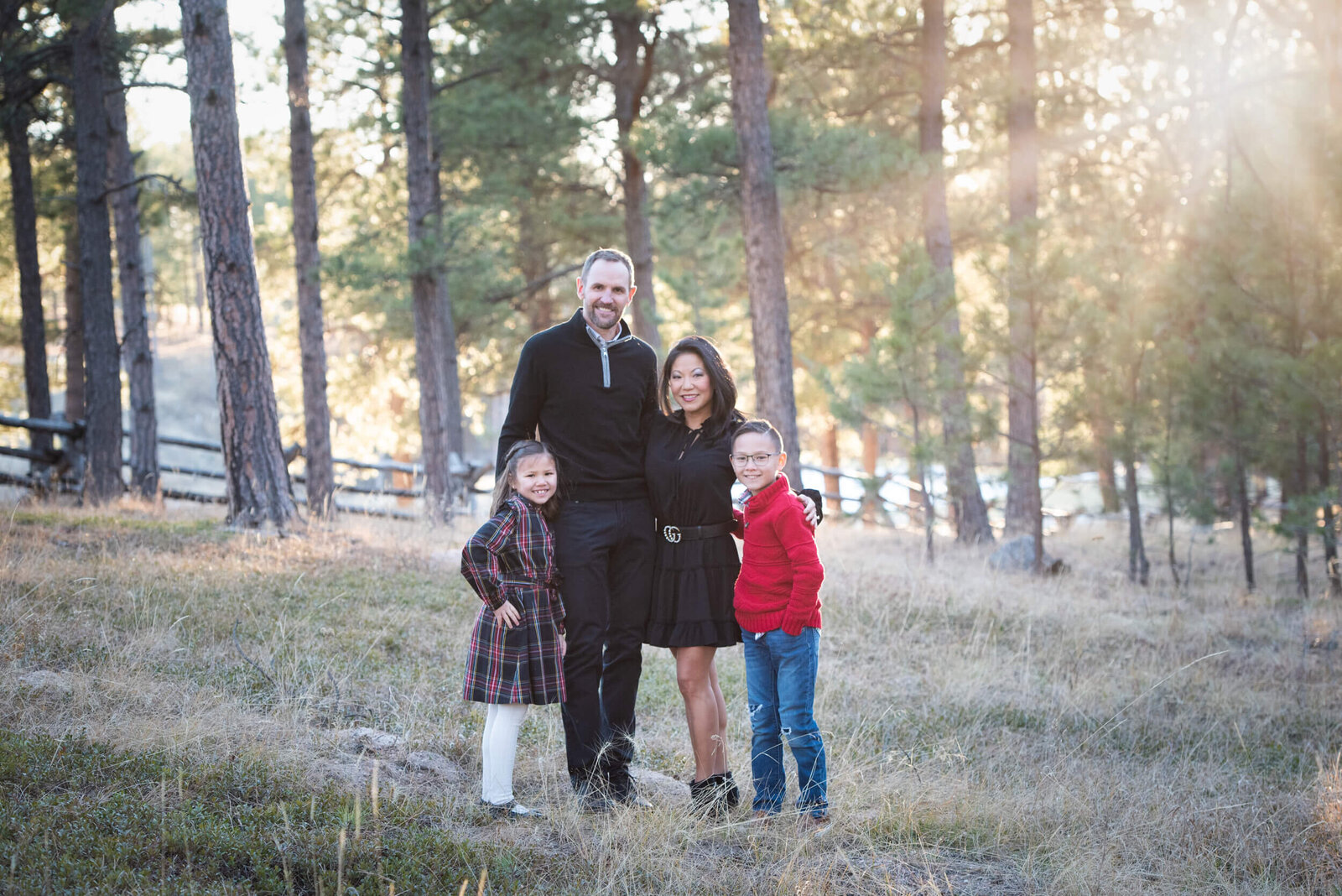 Happy parents stand in a park field at sunset with arms around their toddler son and daughter for a Denver family photographer