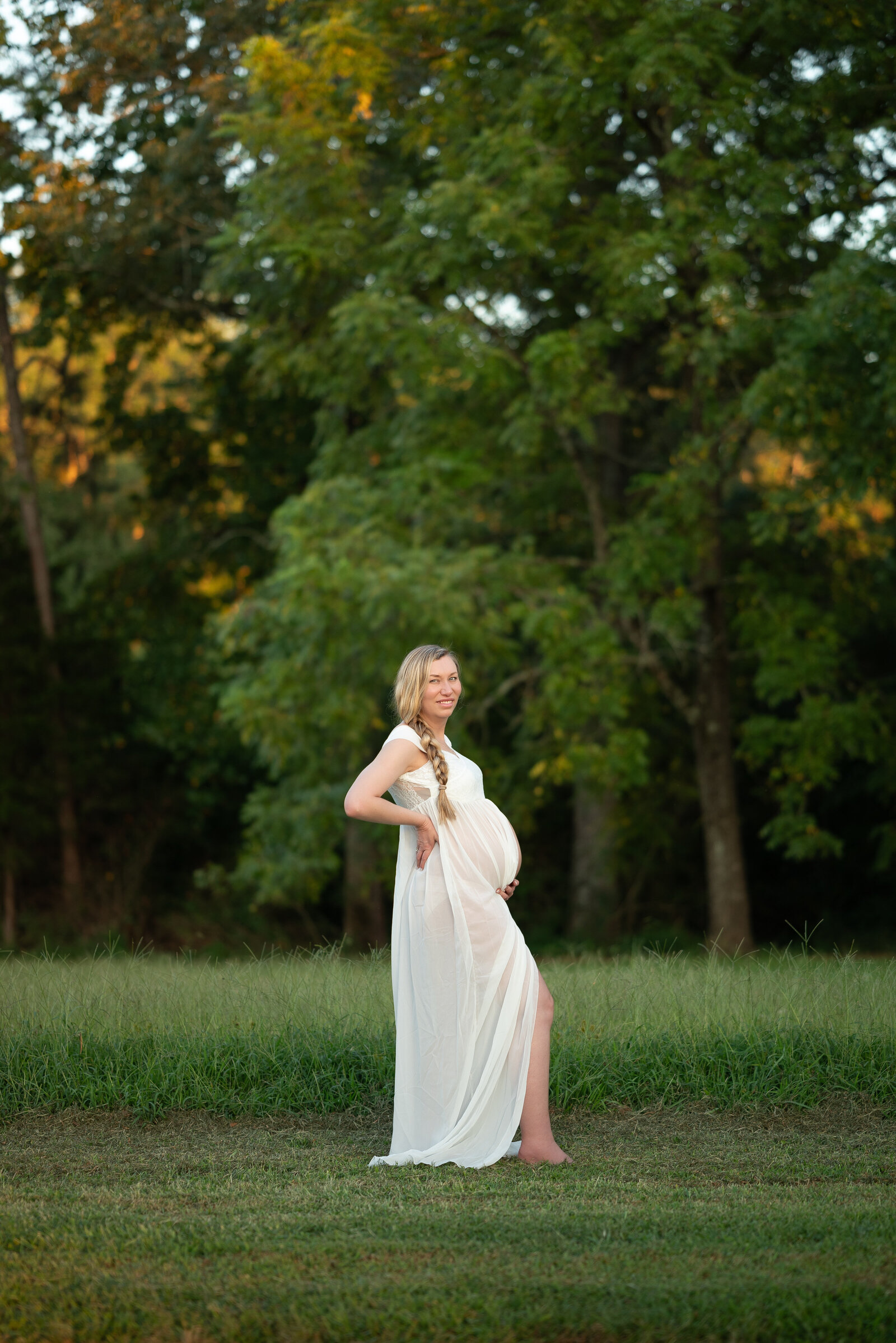 A pregnant woman  with her hand on her stomach and smiling at the camera for her outdoor maternity photos in Huntsville Alabama