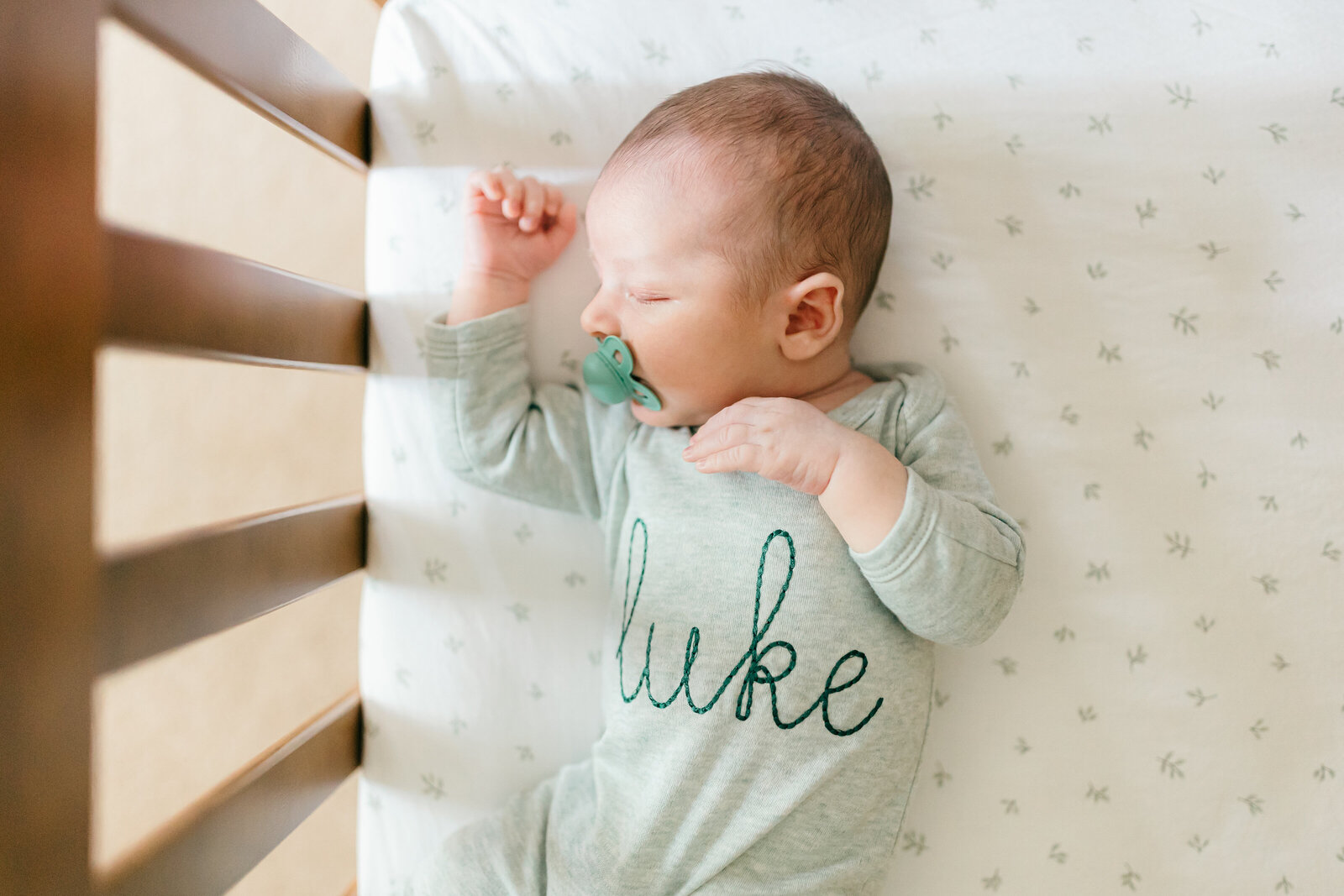 Lifestyle newborn photo in baby boy nursery where he is asleep in his crib wearing embroidered pajamas with his name on them