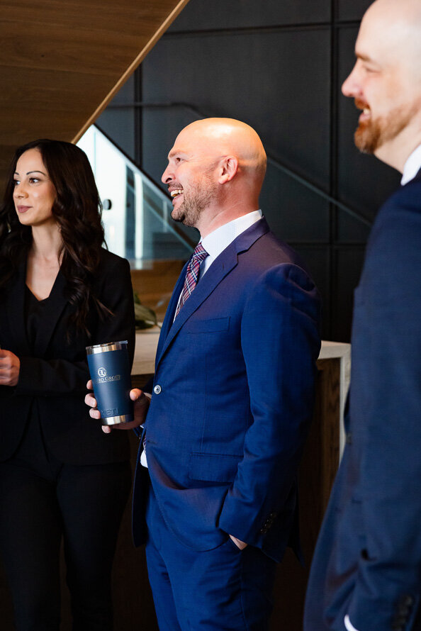 Man in blue suit with a coffee cup laughs with his employees.