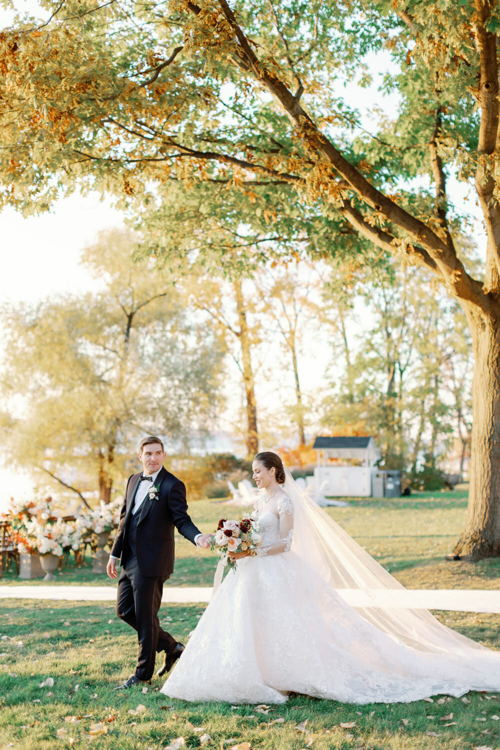 A bride and groom walk across the lawn at Inns of Aurora in the New York fall leaves.