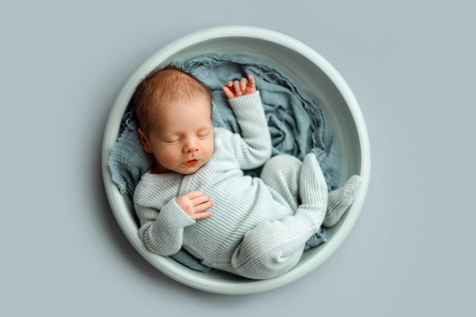 Newborn baby girl swaddled in a white wrap with a delicate headband, cradled in loving hands during a professional newborn photography session in Grand Rapids, Michigan