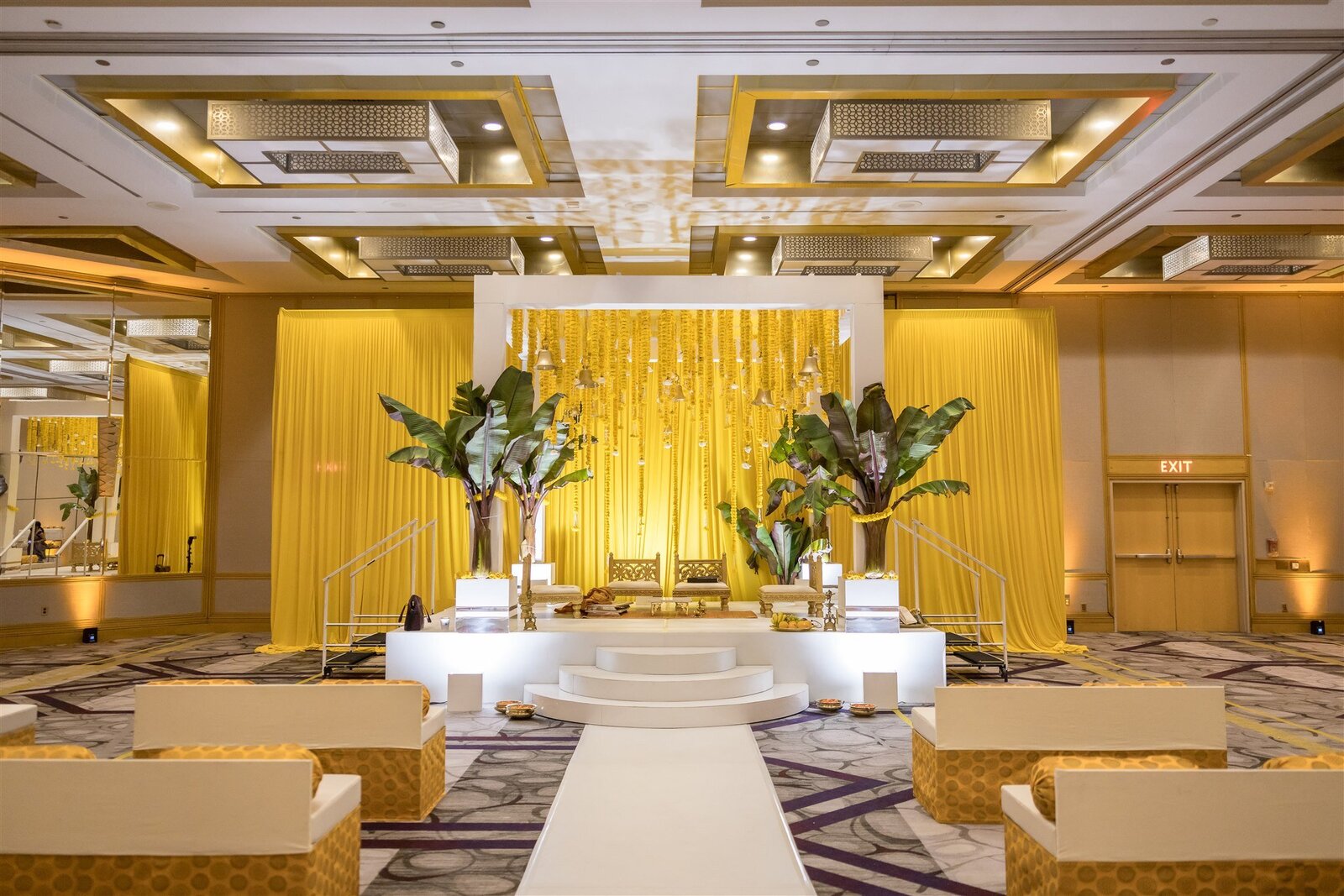 Elegant ballroom wedding ceremony setup with a golden backdrop, white floral arrangements, and soft ambient lighting.