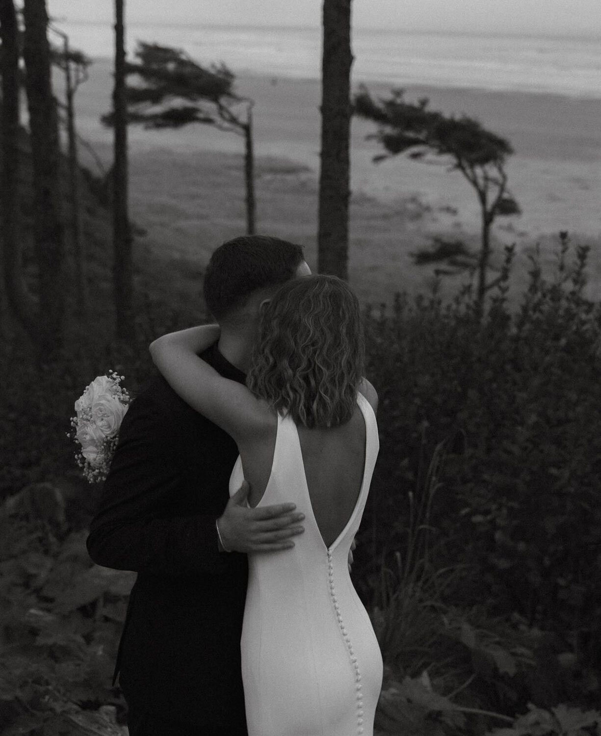 A couple embracing by the coastline, captured in a timeless black-and-white moment