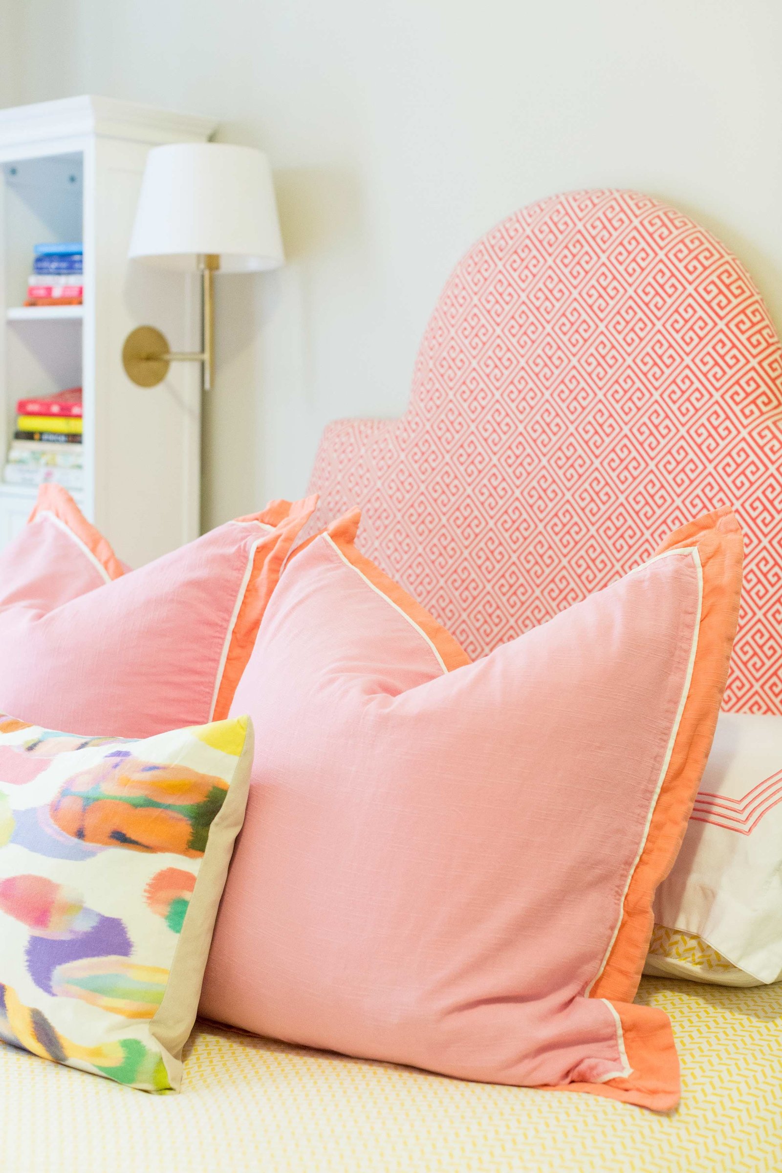 A bed with a pink and orange patterned headboard and pillows.