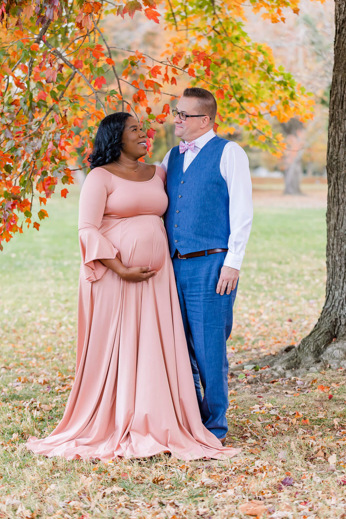 A happy couple standing in a park in Alexandria in the fall during their maternity photo session.