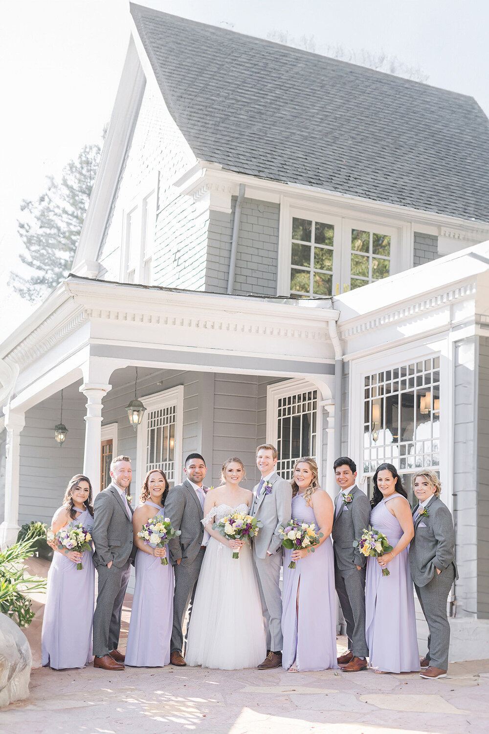 a wedding party poses and smiles in front of the wedgewood sequoia mansion wedding venue in placerville, CA