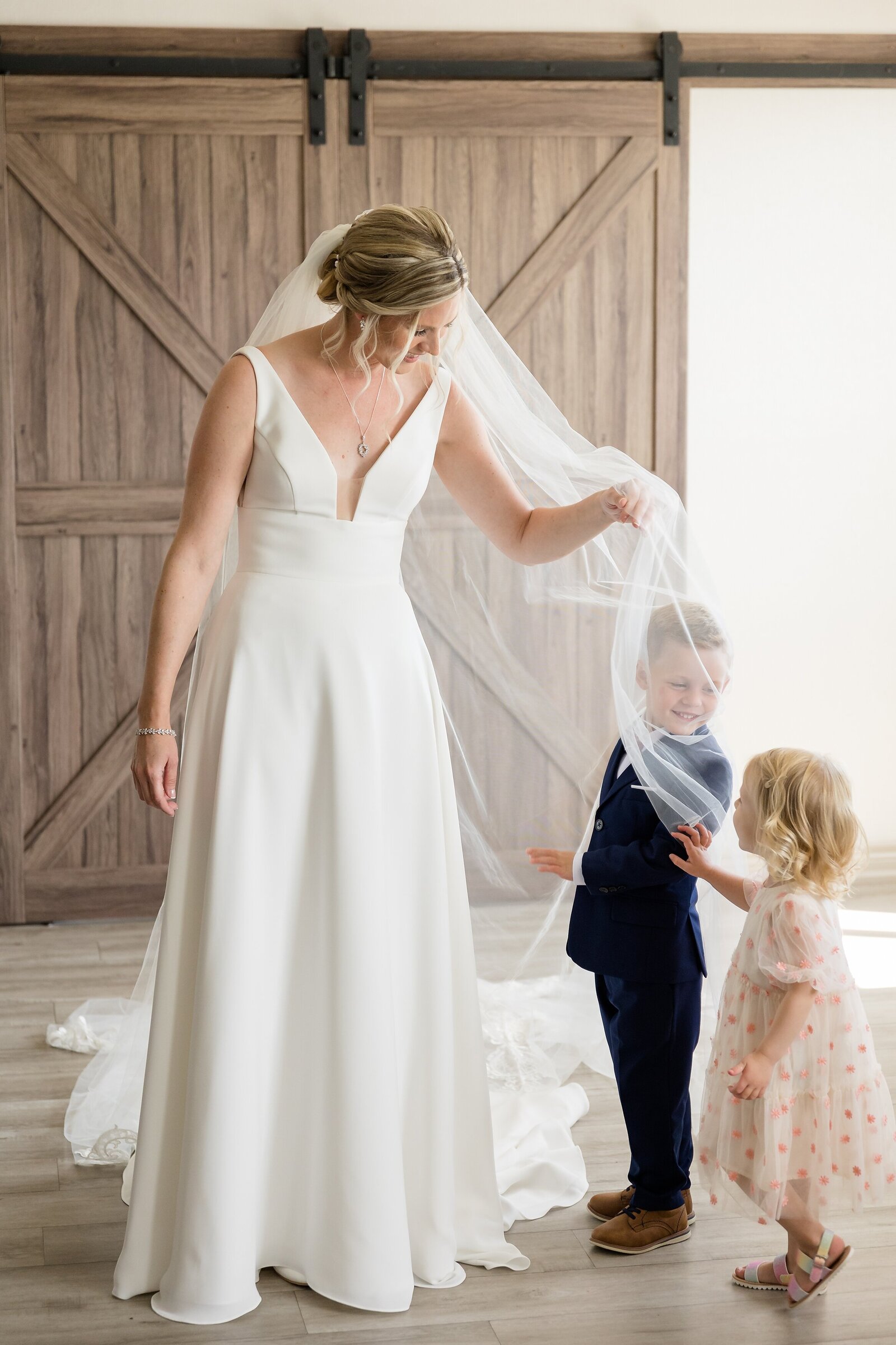 Ring-bearer-and-flower-girl-play-under-brides-veil-on-her-wedding-day-during-getting-ready
