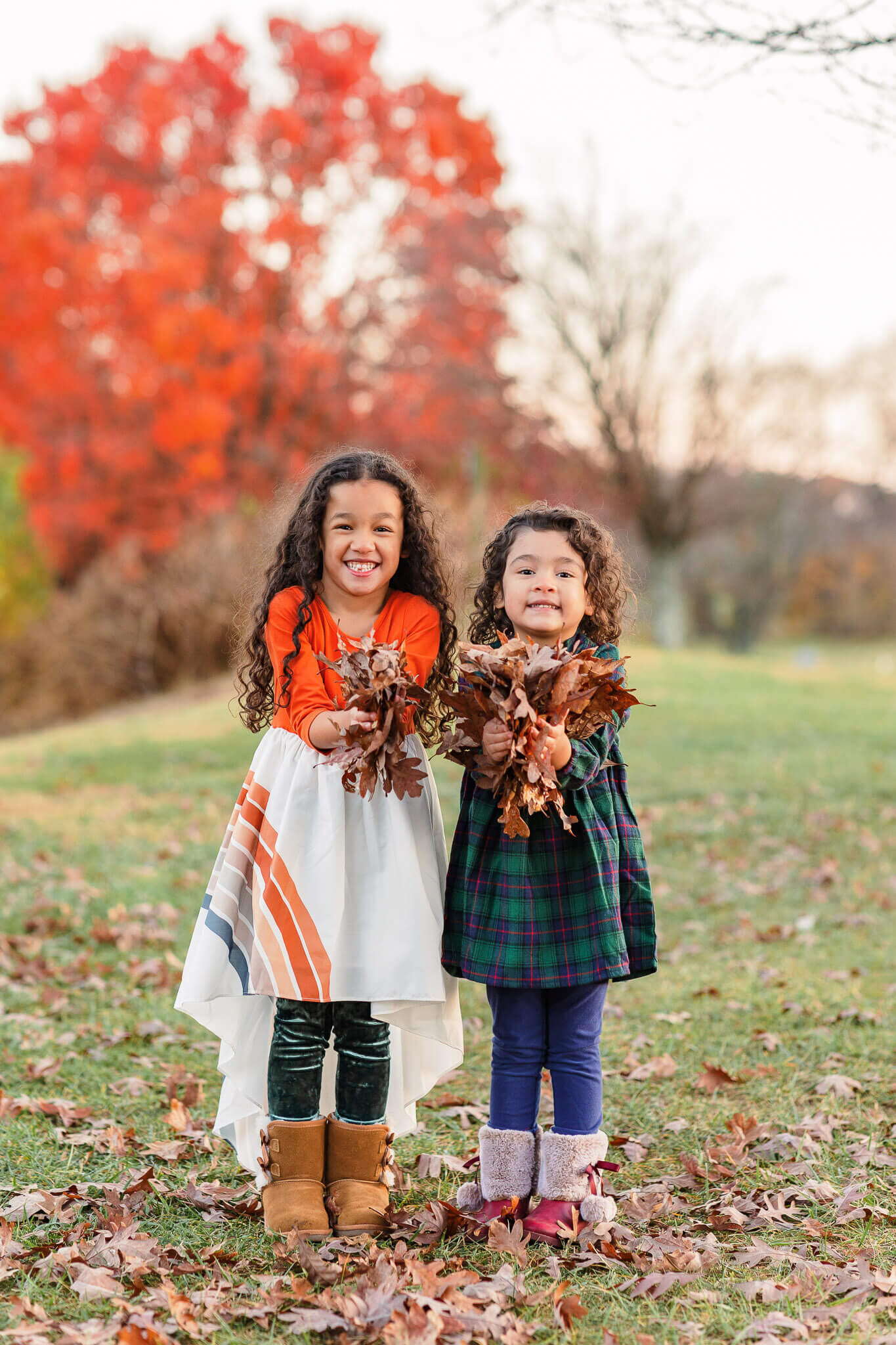 Two little girls holding a pile of leaves getting ready to throw