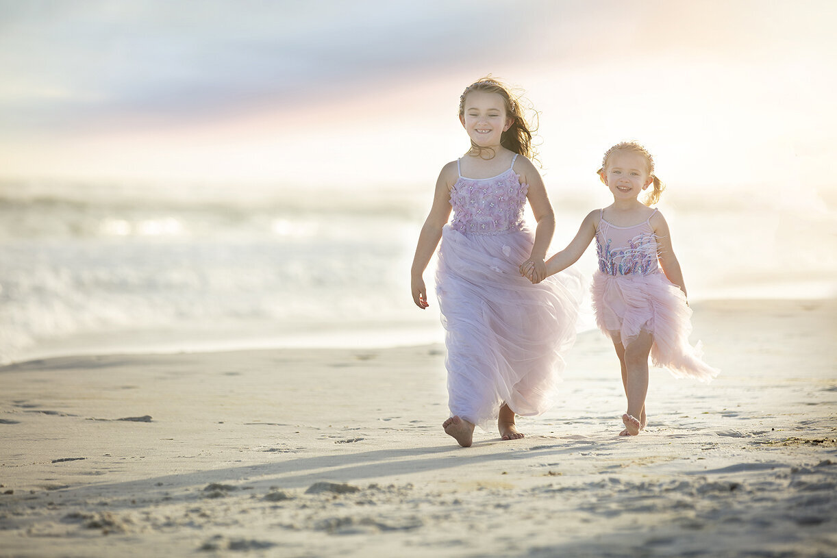 Sisters holding hands walking on the beach with a Dallas child photographer.