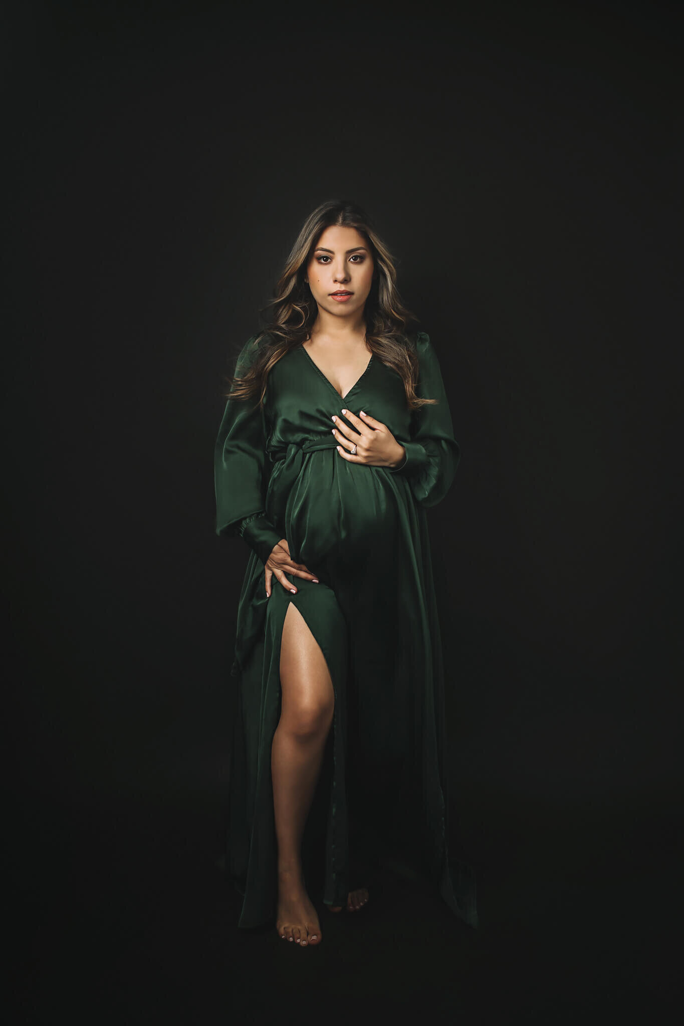 Powerful picture of a pregnante woman wearing a green dress in a black background