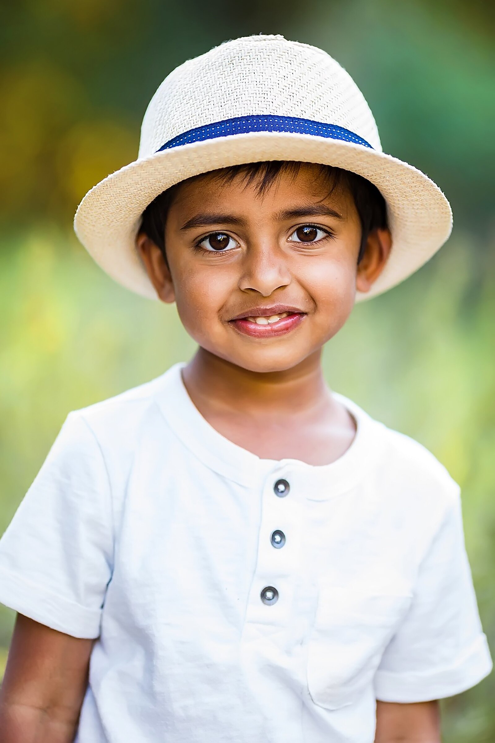young boy smiling in a field and wearing a hat