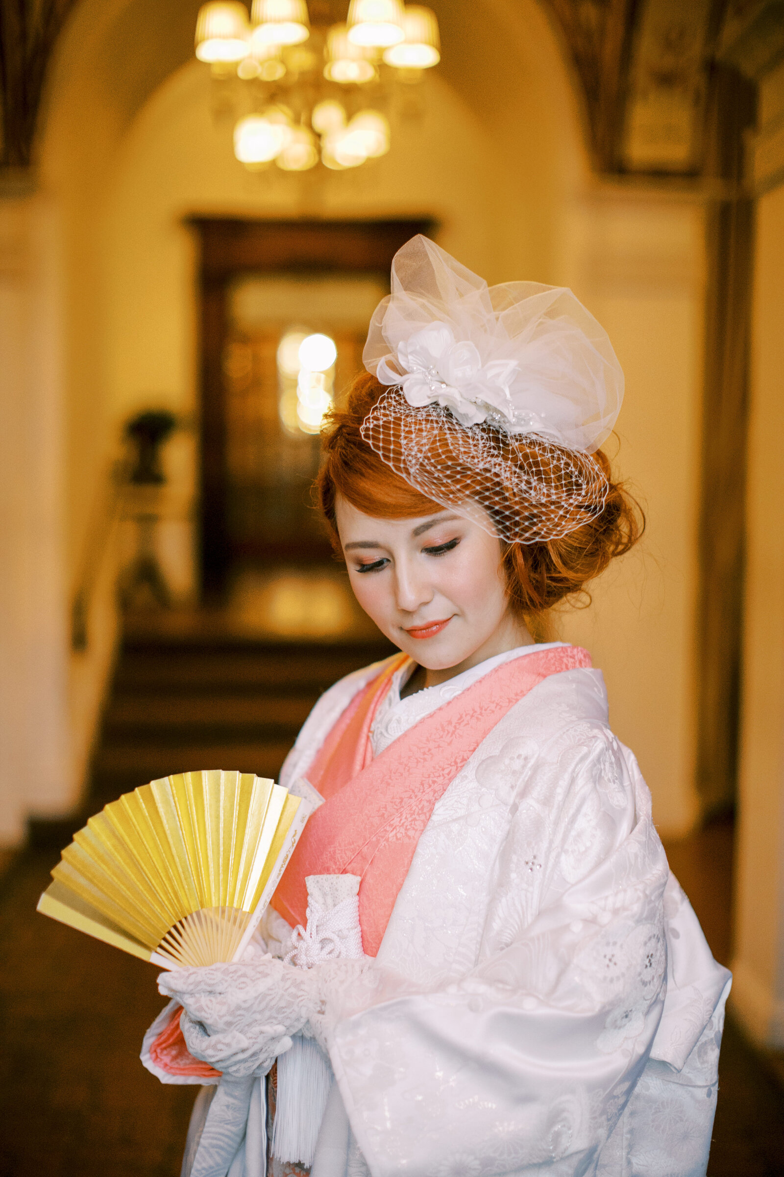 Bride holding a golden fan wearing white shiromuku wedding kimono with soft pink accents at Carondelet House, Los Angeles California, ideal for wedding kimono rental | 金扇子を手に白無垢と淡いピンクの掛下を合わせた花嫁 カロンデレットハウス ロサンゼルス カリフォルニアで着物レンタル可能
