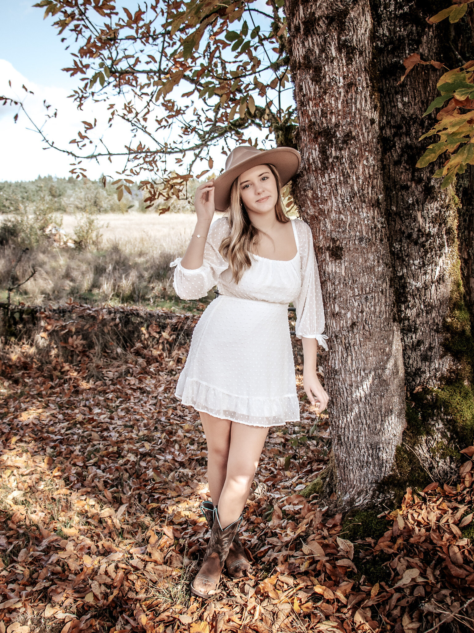 High School Senior girl, leaning against a tree playing with her hat