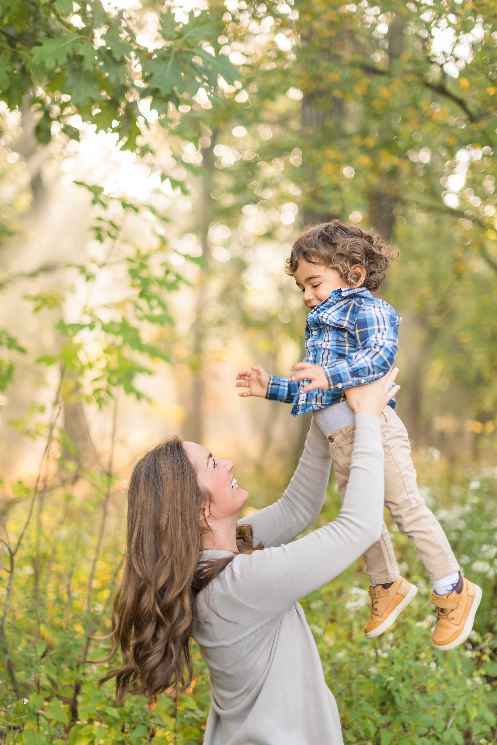 Mom throwing her toddler son in the air in the sunny fall woods