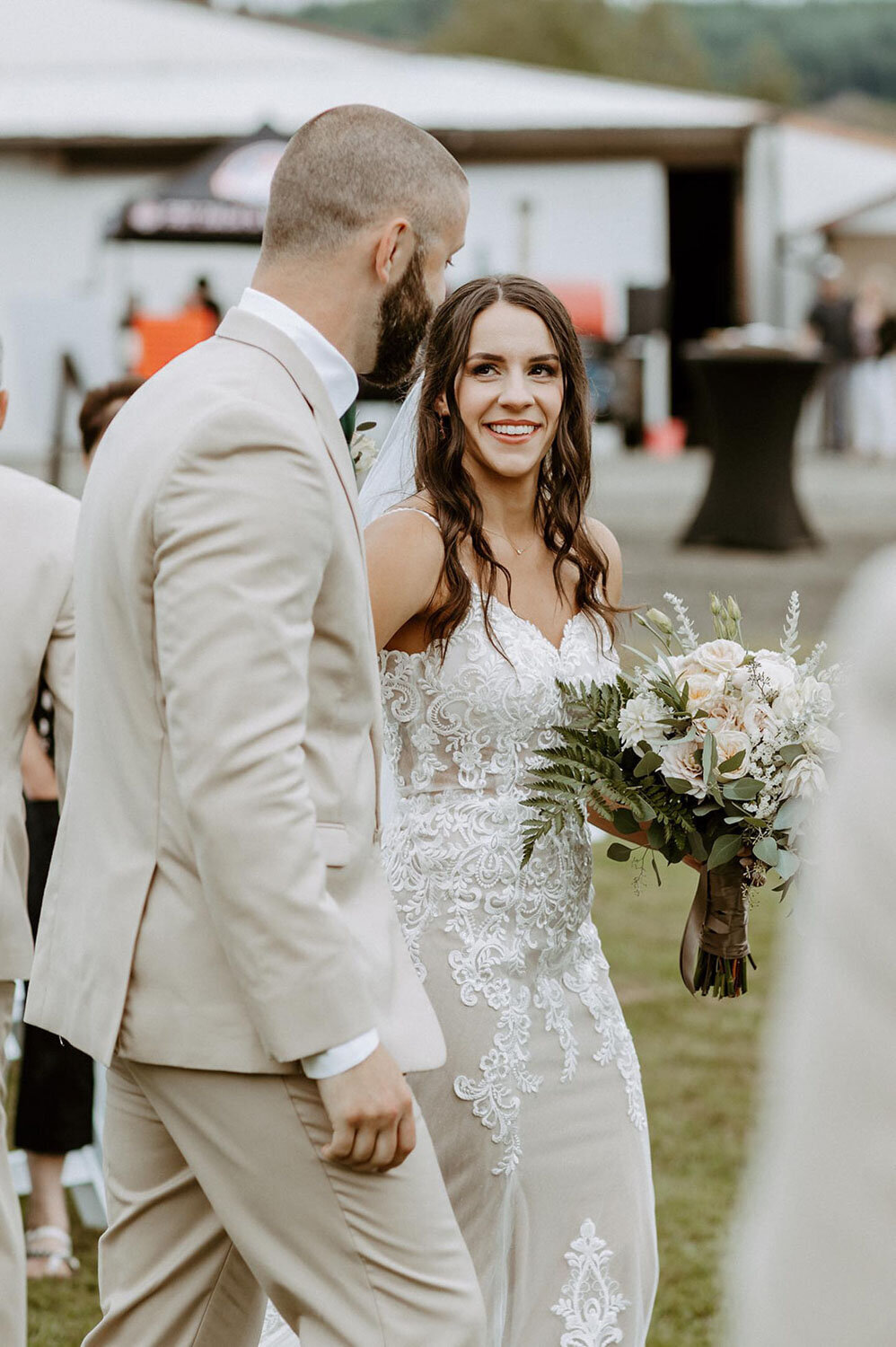 A bride walking with her groom, holding a bouquet and smiling warmly