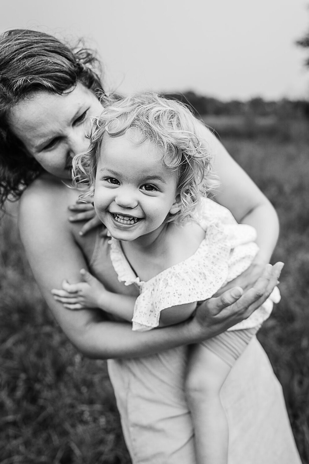 toddler girl smiles wide at camera in moms arms