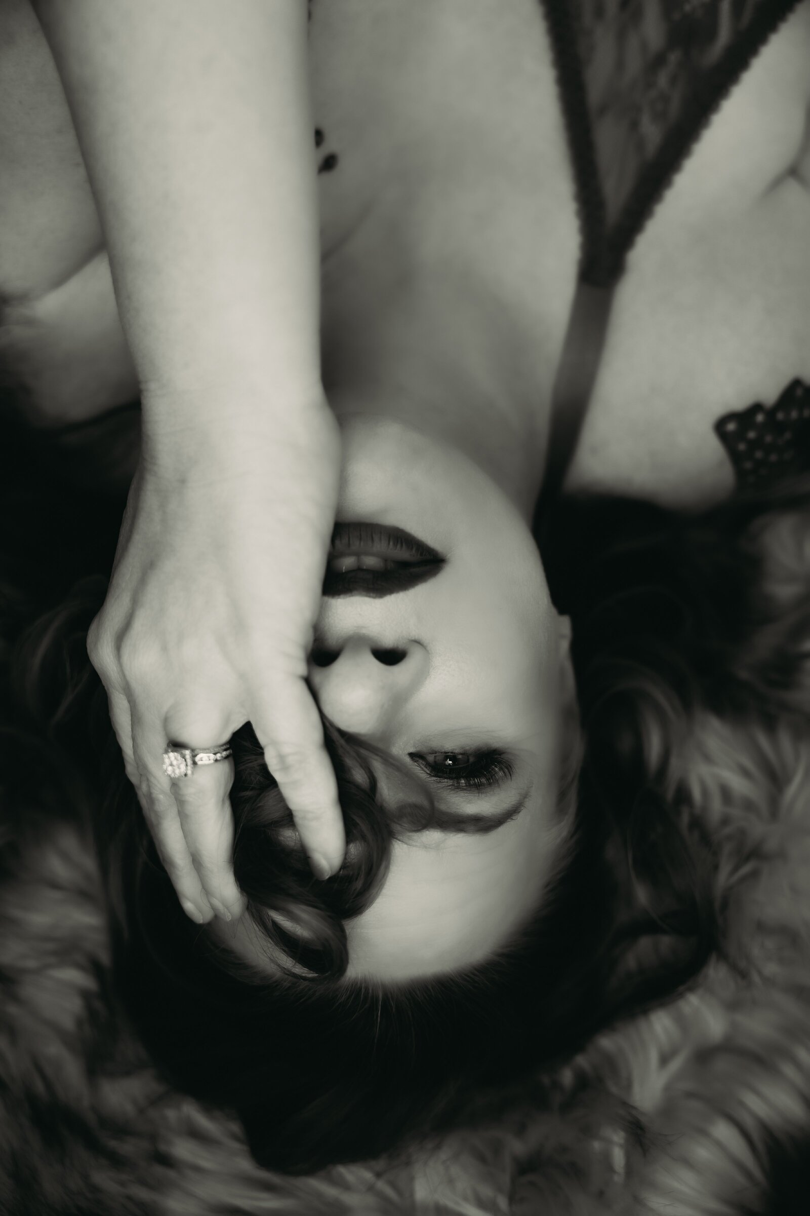 Close up in black and white upside down of women looking at the camera holding some of her hair  to cover her left eye