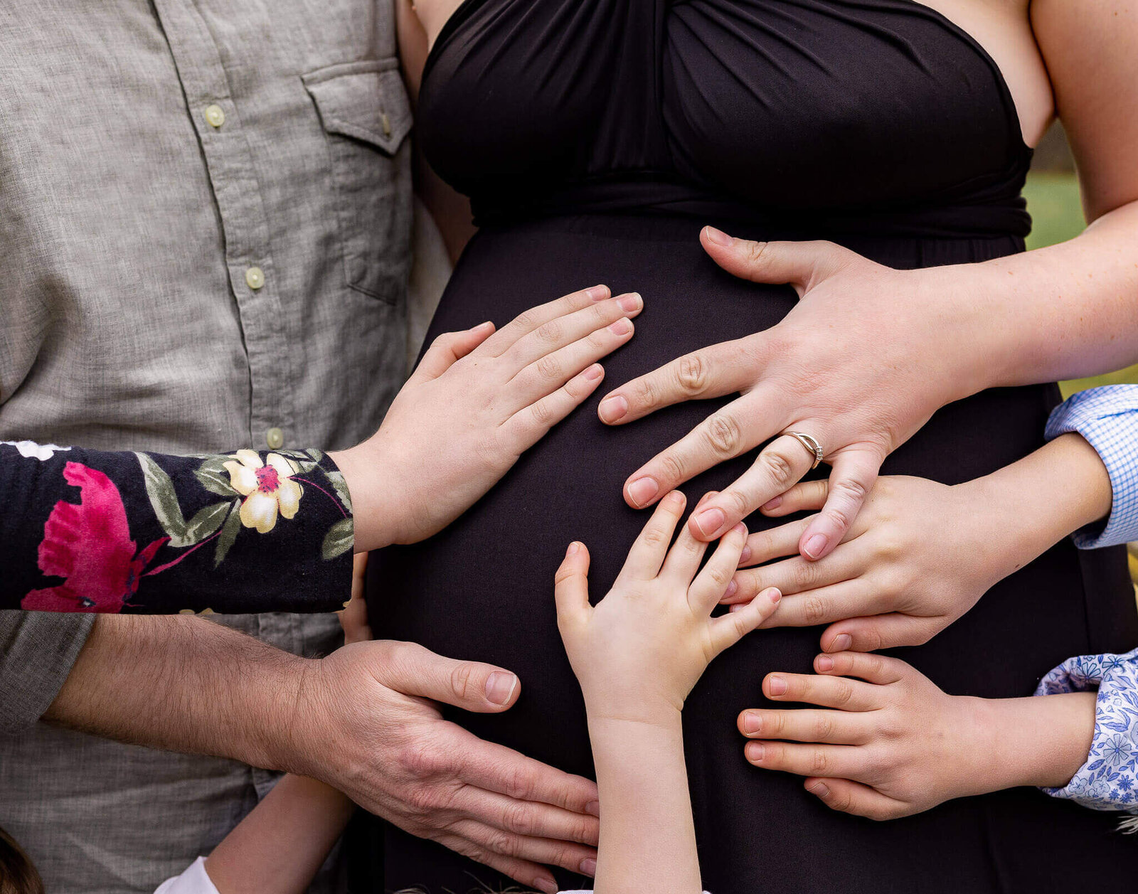 A close-up of a pregnant woman's belly with seven hands holding the bump at a Chantilly maternity session.