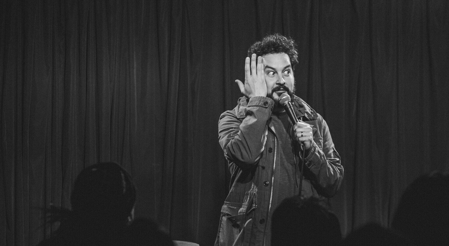 Ahmed Bharoocha on stage, holding a microphone, and placing his hand against his face